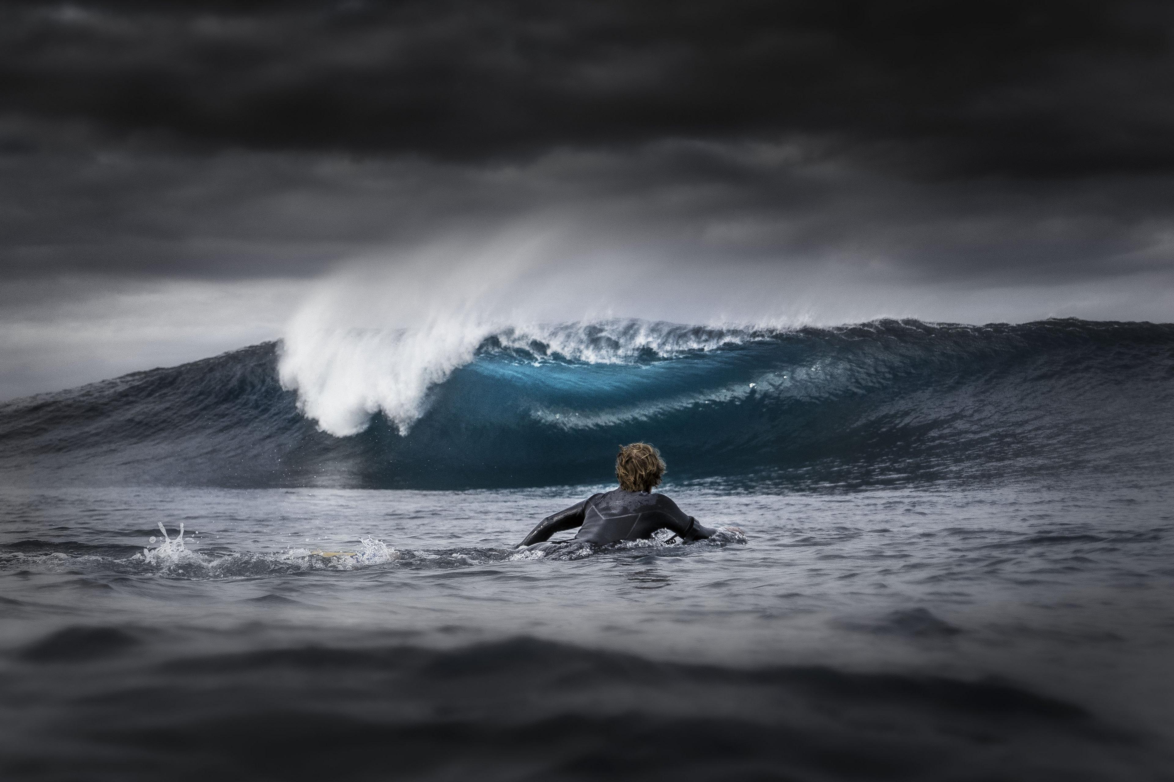 A bodyboarder paddling out to sea while big storm clouds block the sun.