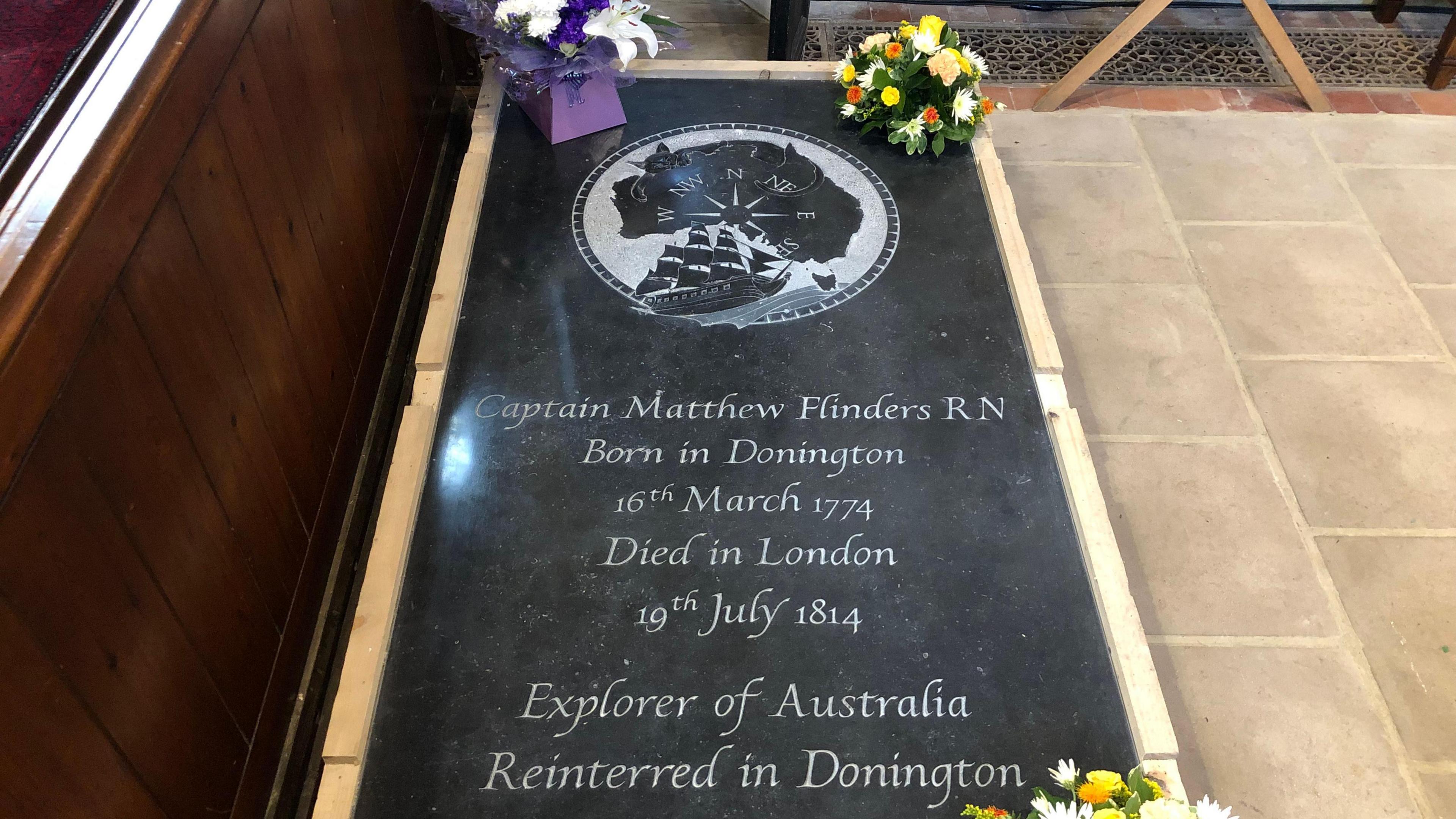 A black marble gravestone with ship and compass motif for Matthew Flinders, within Donington church. The text on the gravestone reads: Captain Matthew Flinders R.N., Born in Donington 16th March 1774, died in London 19th July 1814. Explored of Australia, Reinterred in Donington.