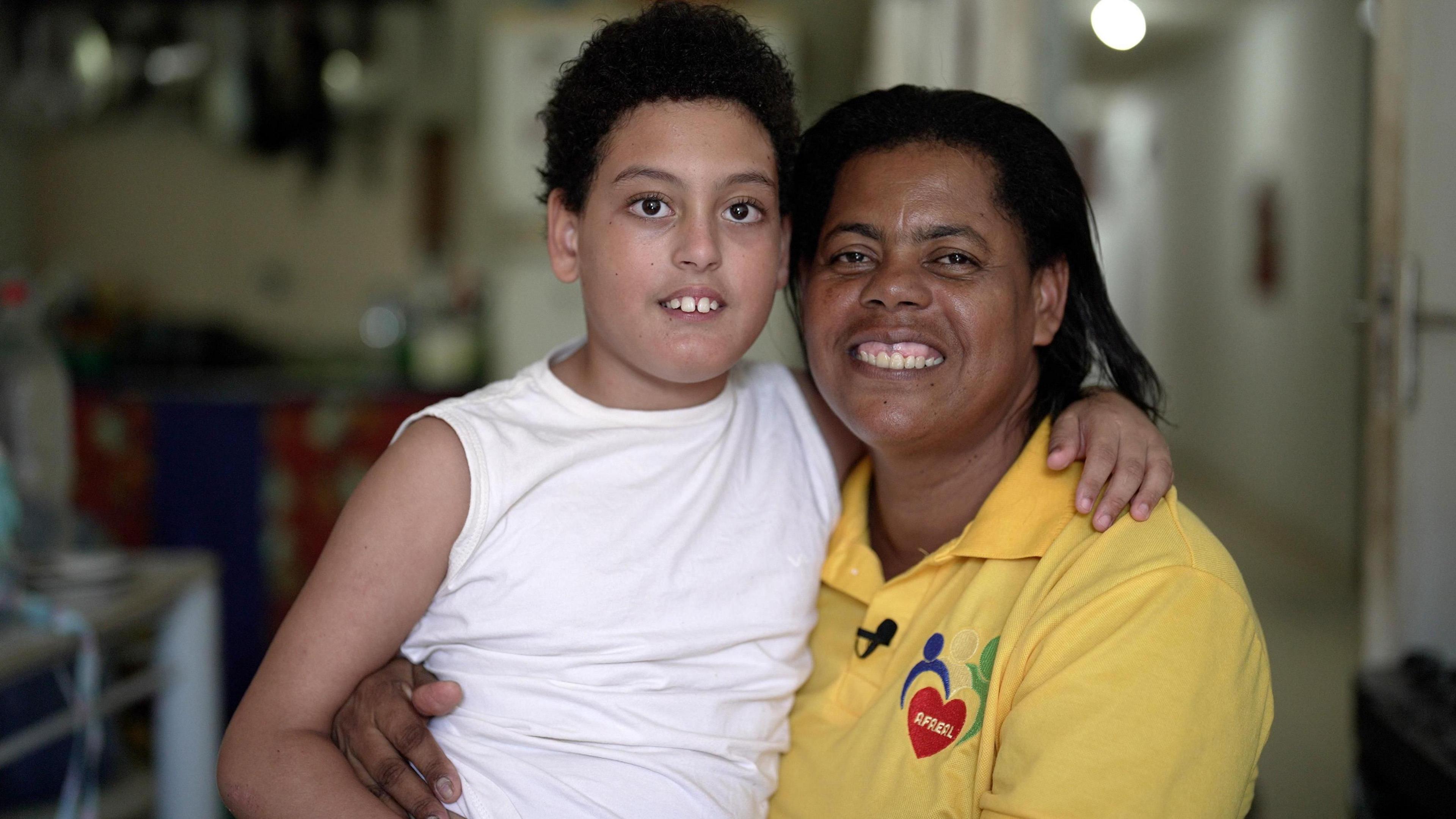 Enzo and Lenice França smile at the camera. Lenice is wearing a yellow polo shirt and Enzo is wearing a white vest.