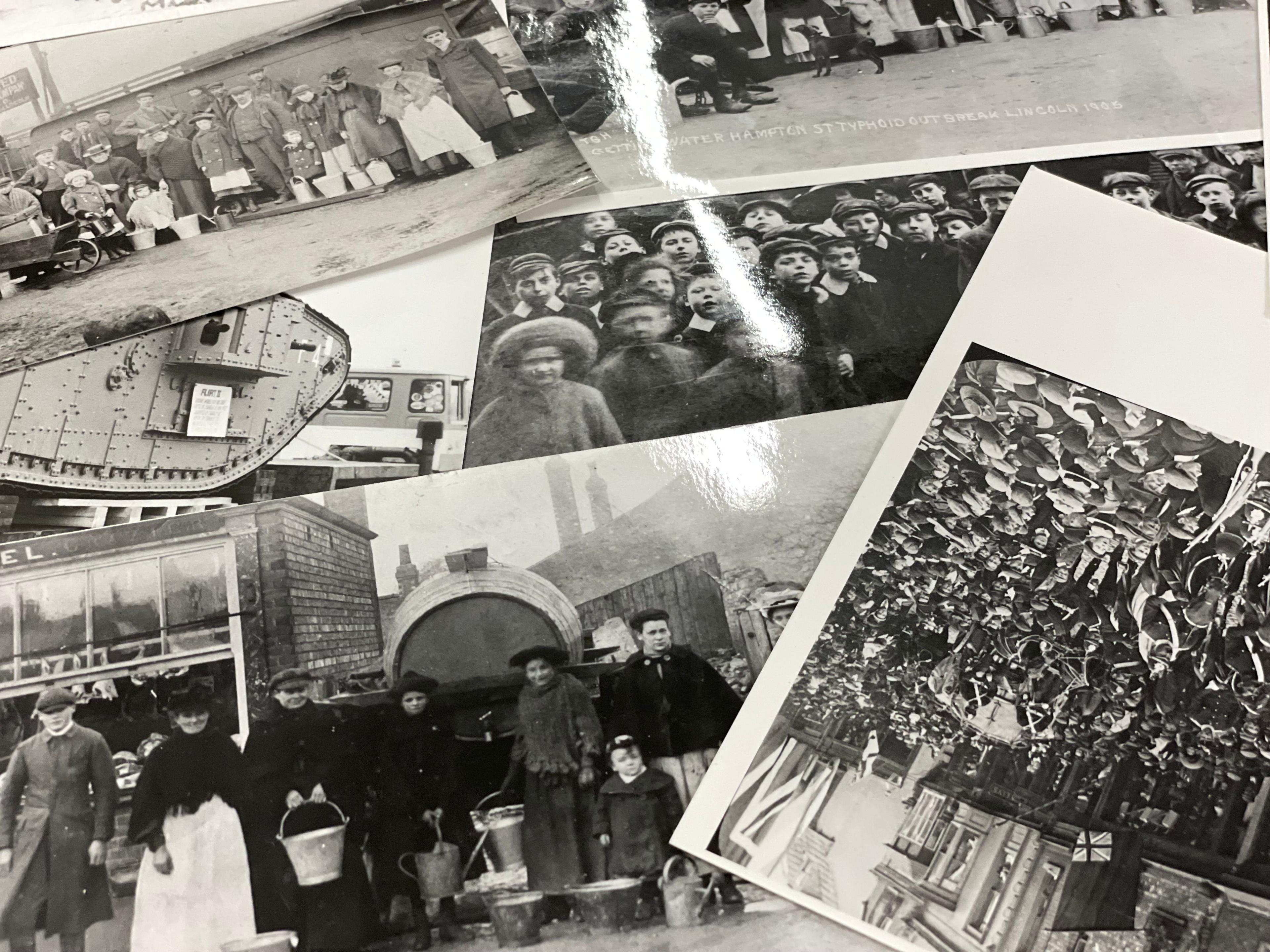 Six black-and-white photos spread across a table, showing various groups of people, including schoolchildren, all dressed in the clothes of the early 20th century. A caption on one mentions a typhoid outbreak of 1905. Another photo shows a World War One tank.