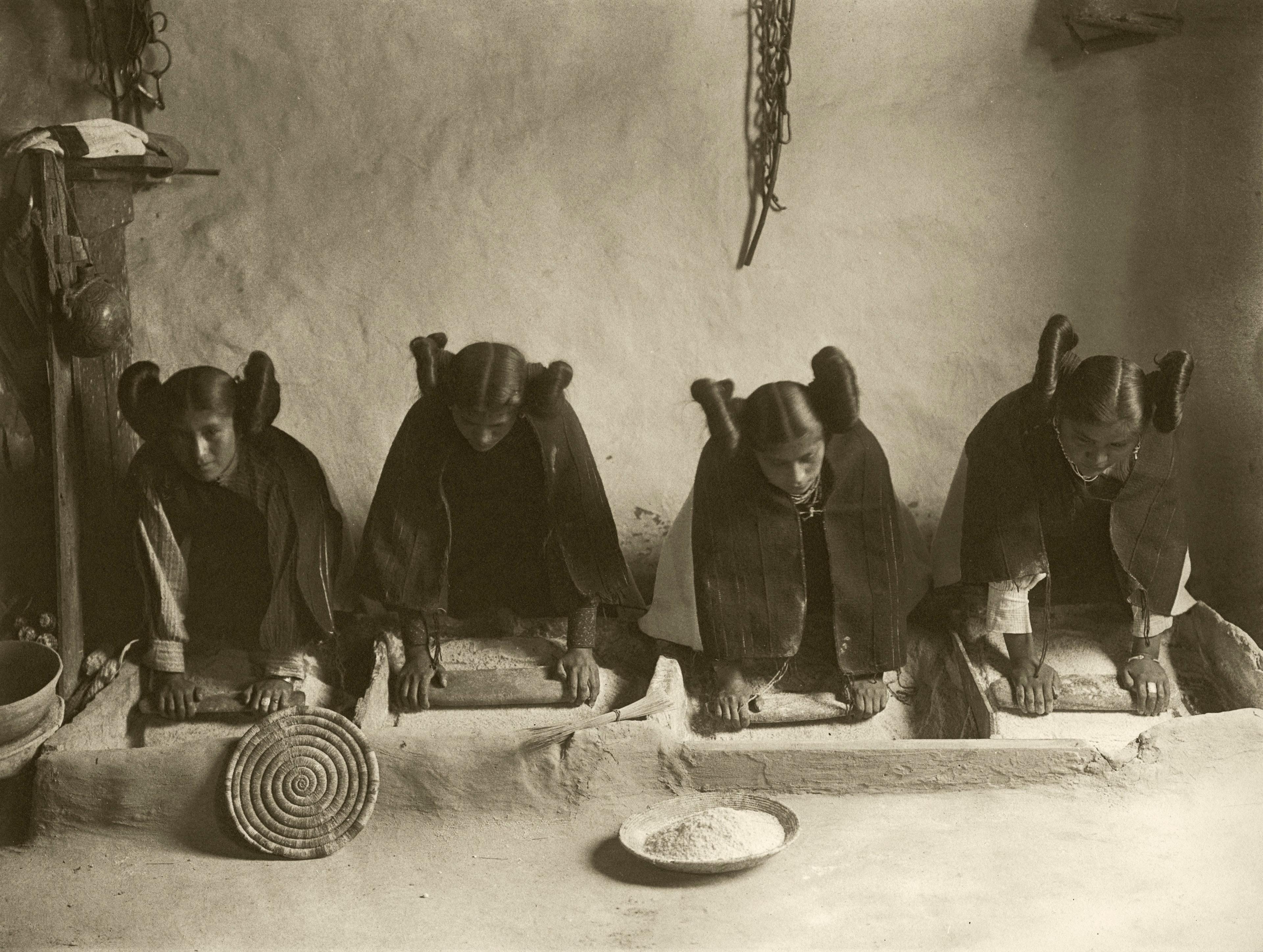 Hopi women grinding grain in a mealing trough.