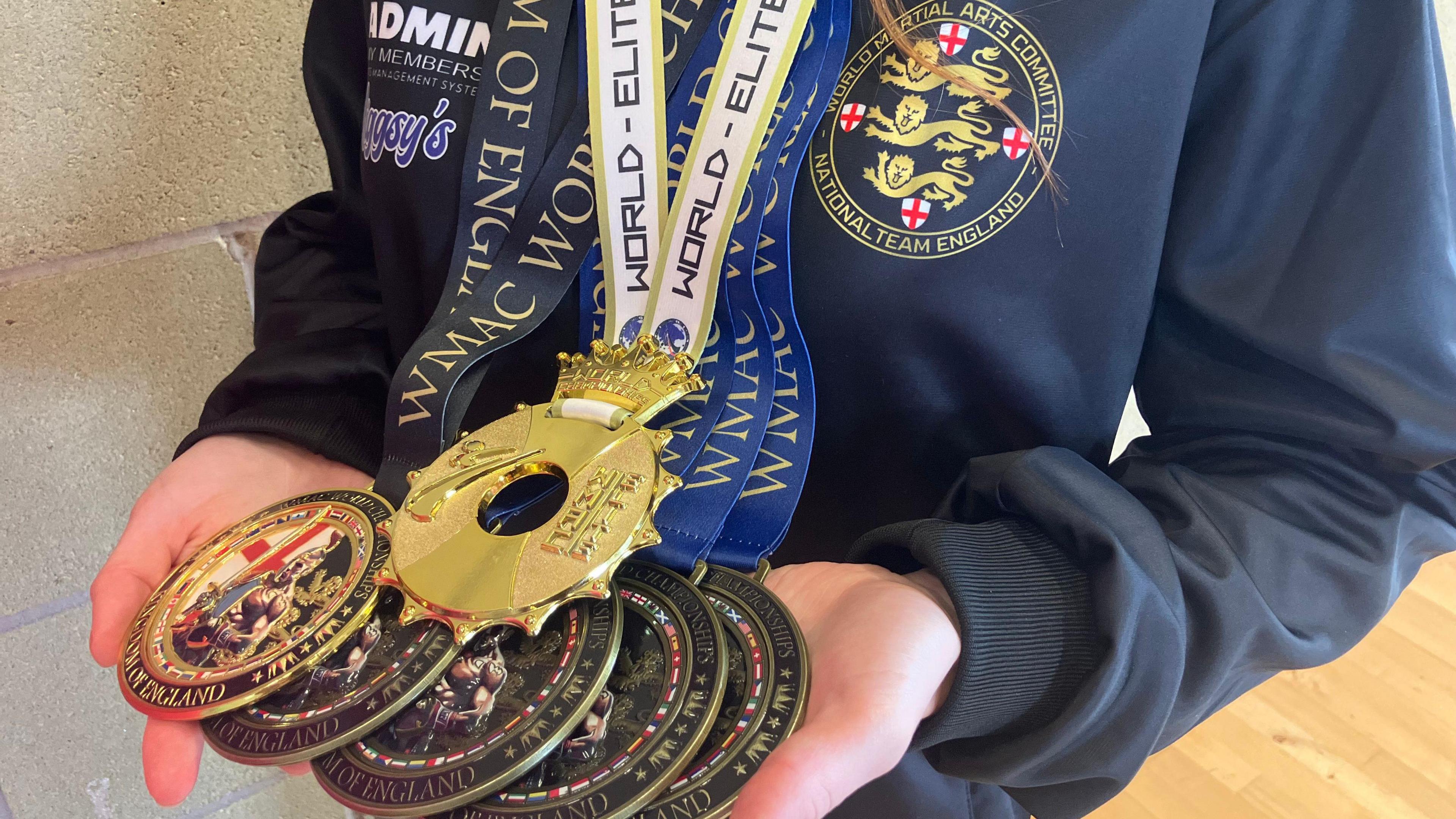 A close up of Lana's two hands cradling the six medals. She is wearing a navy blue England branded hooded jumper.