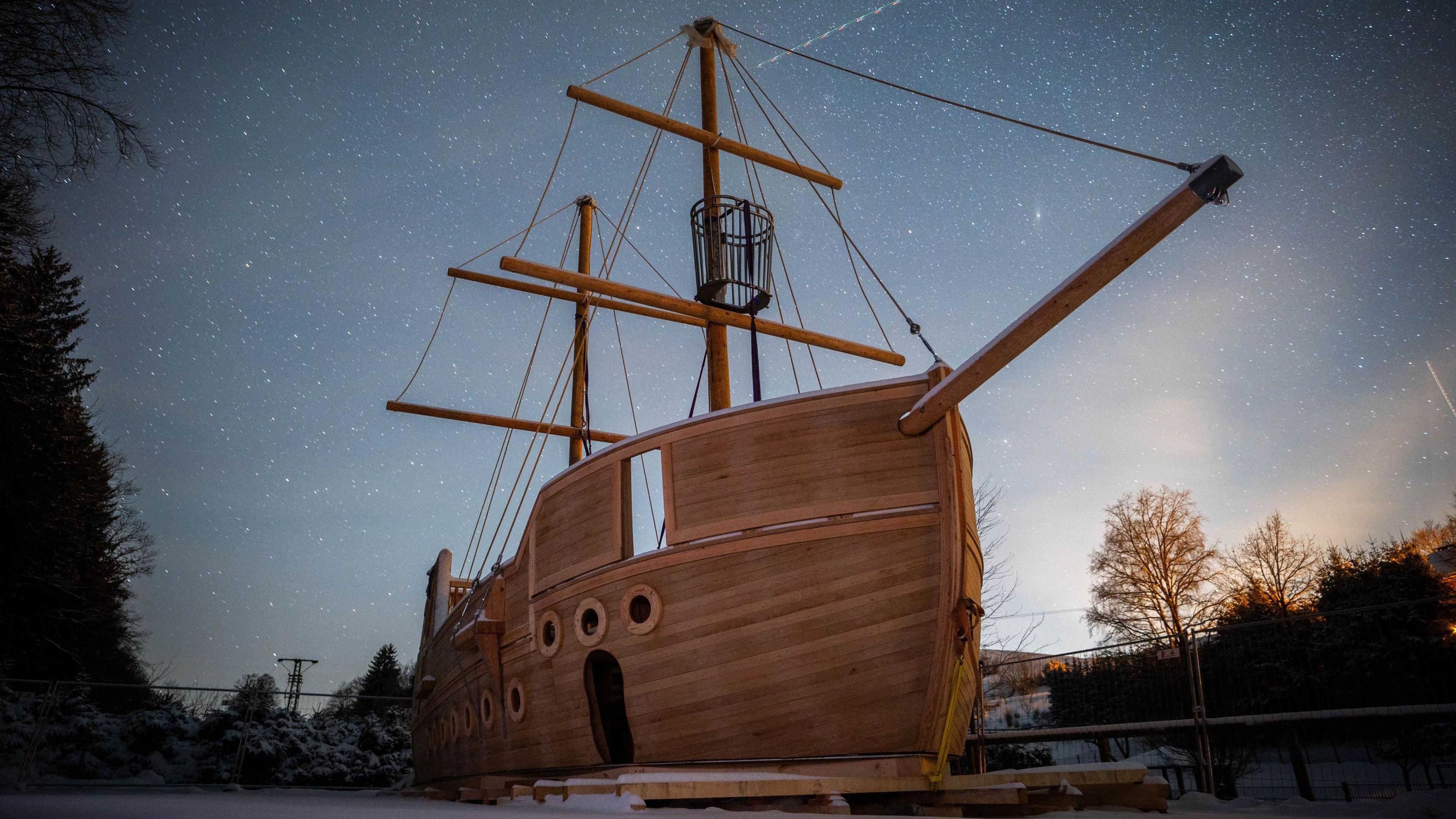 A partially constructed wooden miniature galleon against a starry sky. 