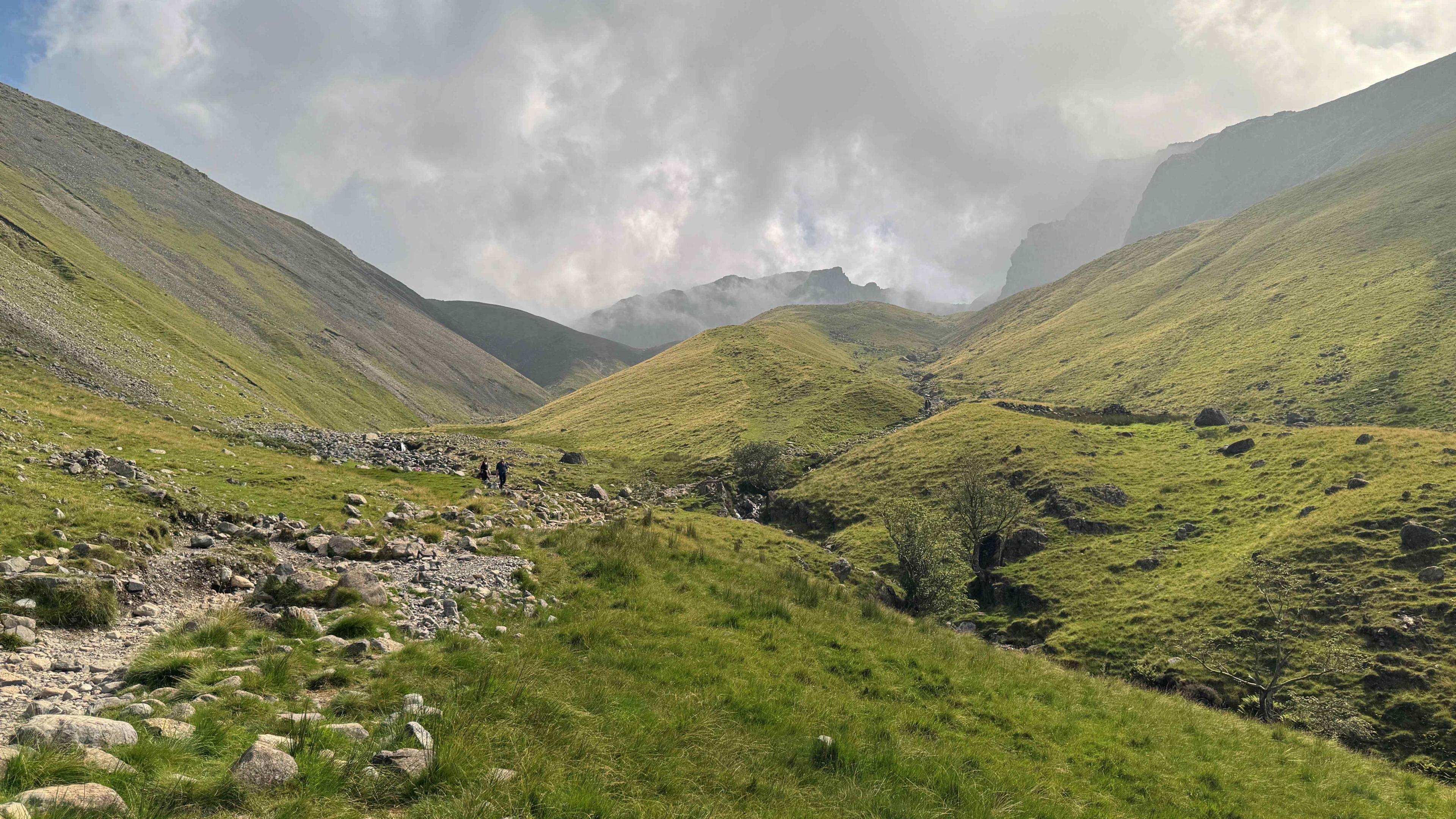 A general view of the route up to Scafell Pike in the Lake District. The rugged path is surrounded by the green fells with low grey clouds surrounding the tops.