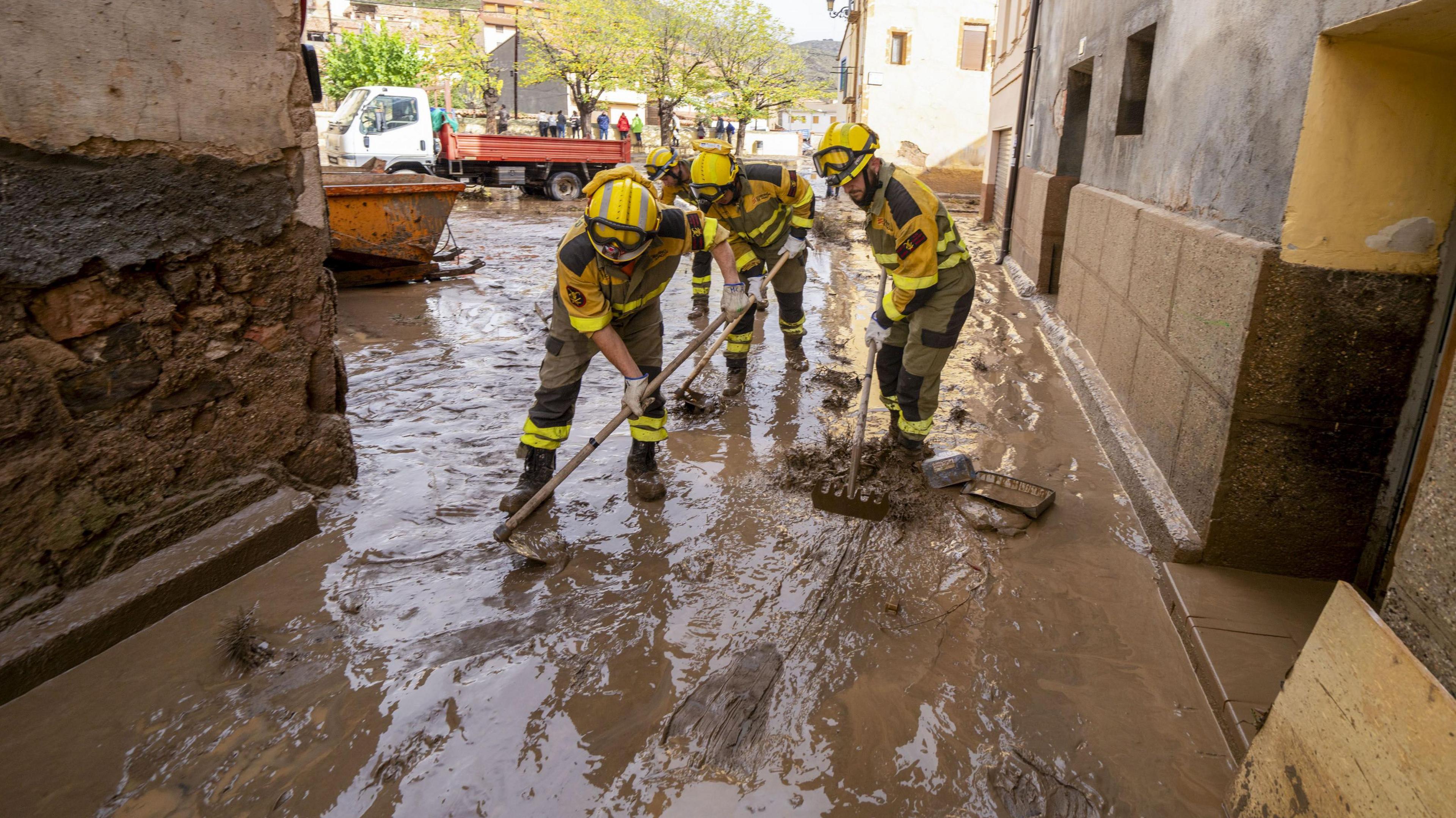 Emergency crews wearing yellow uniforms try to clean streets covered in muddy water after flash flooding in Spain. 