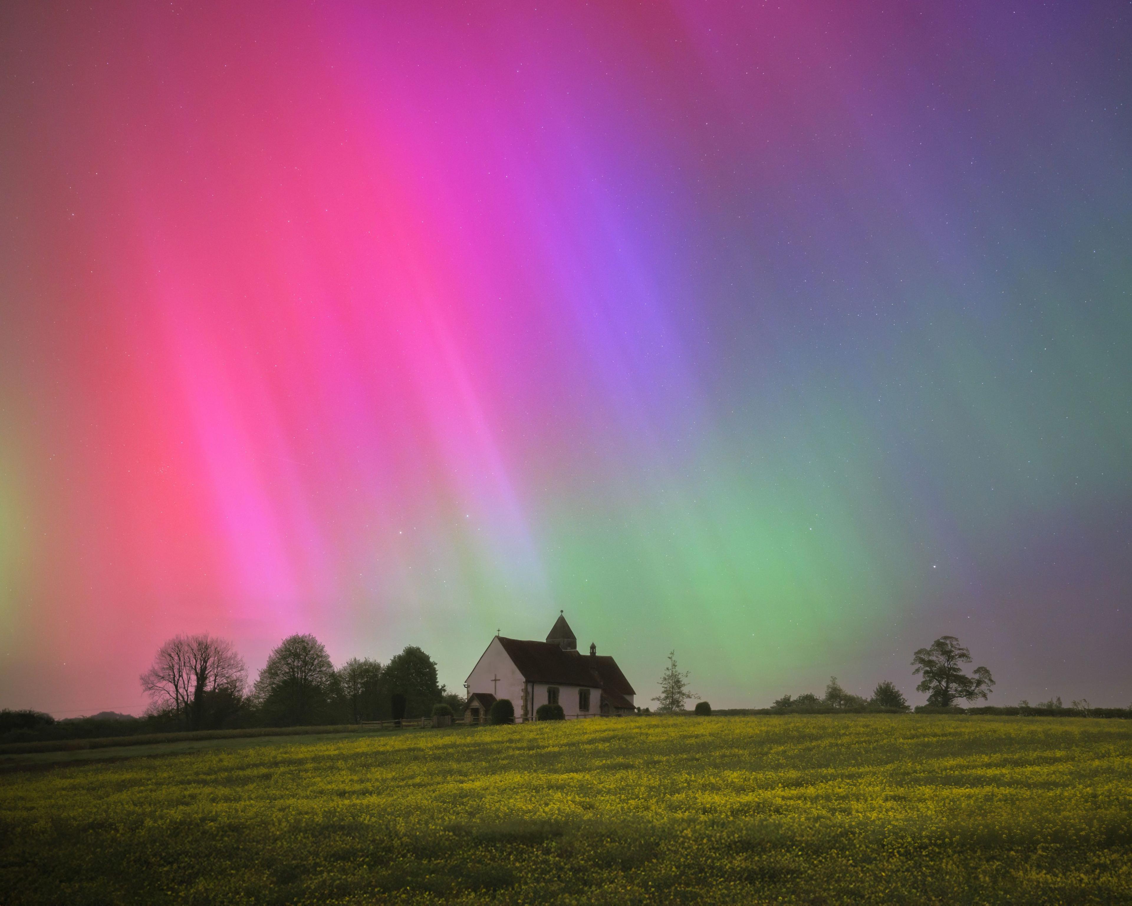 pink and green northern lights above a building on a field.