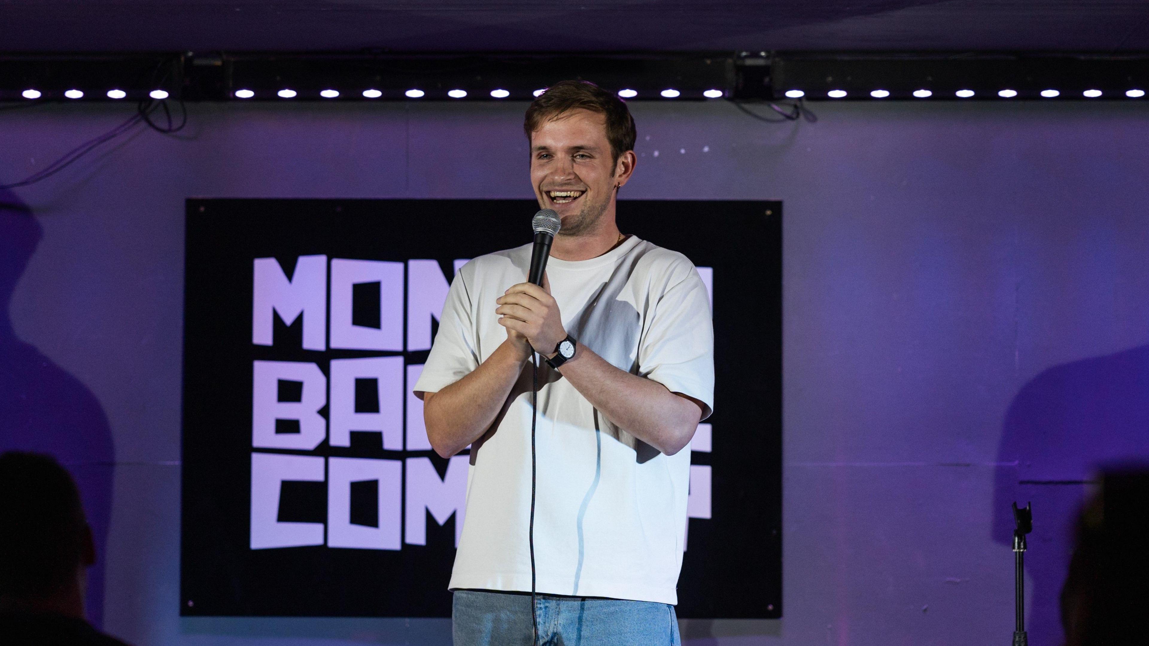 Vittorio Angelone stands on stage in a white t-shirt, holding a microphone