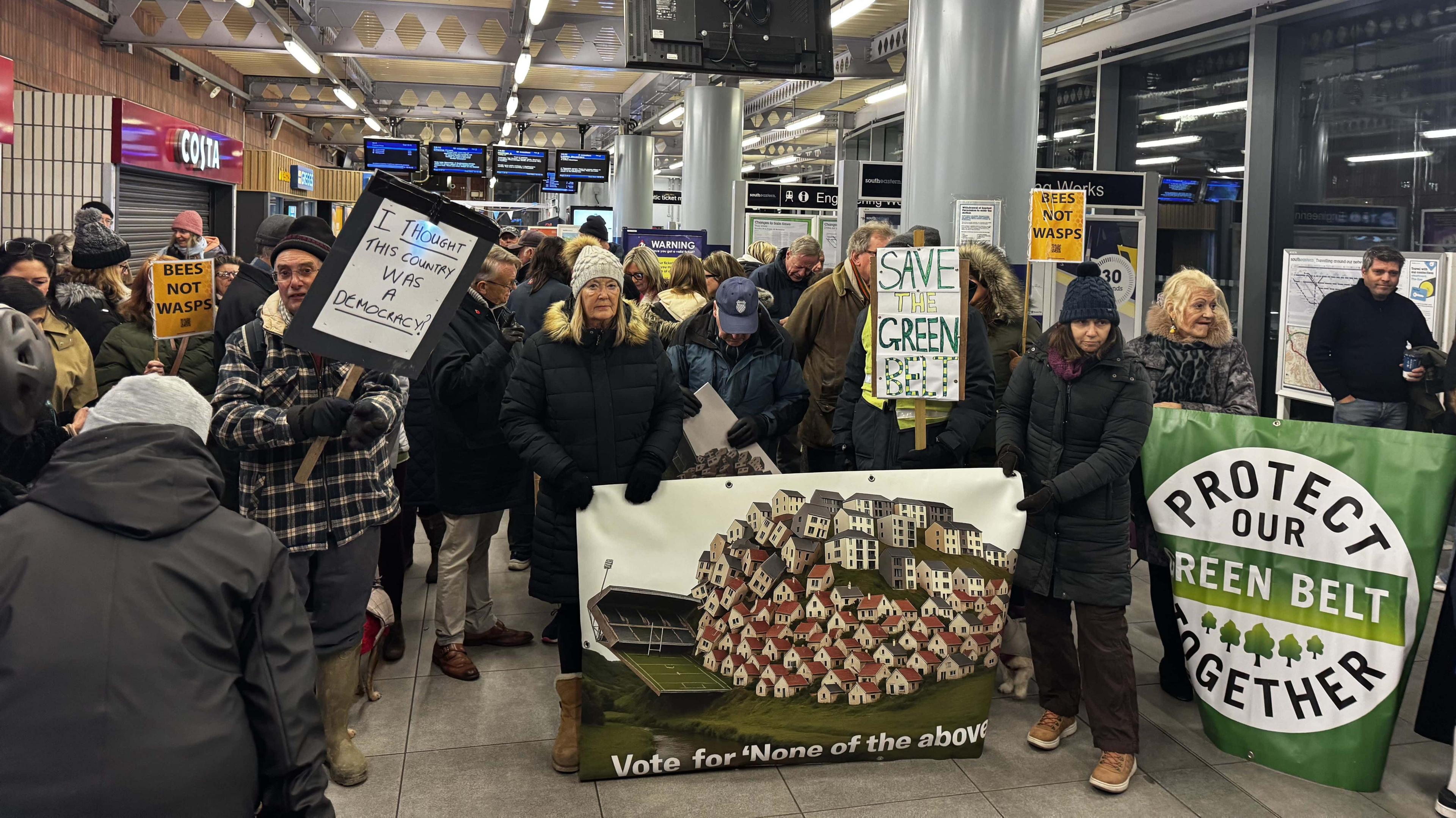 Protestors gather in the concourse of Sevenoaks train station with banners about protecting the green land