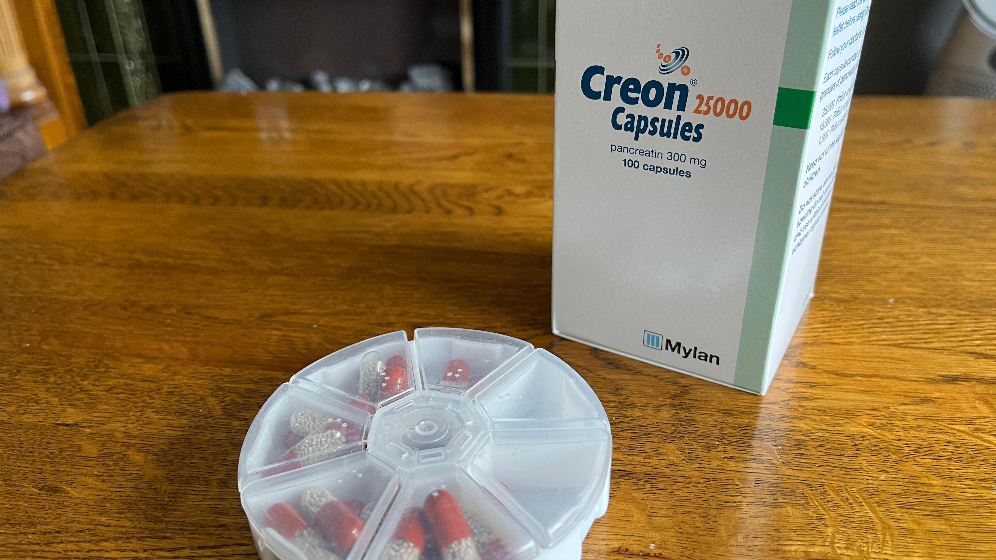 Creon capsules in a pill caddy next to a box of Creon 