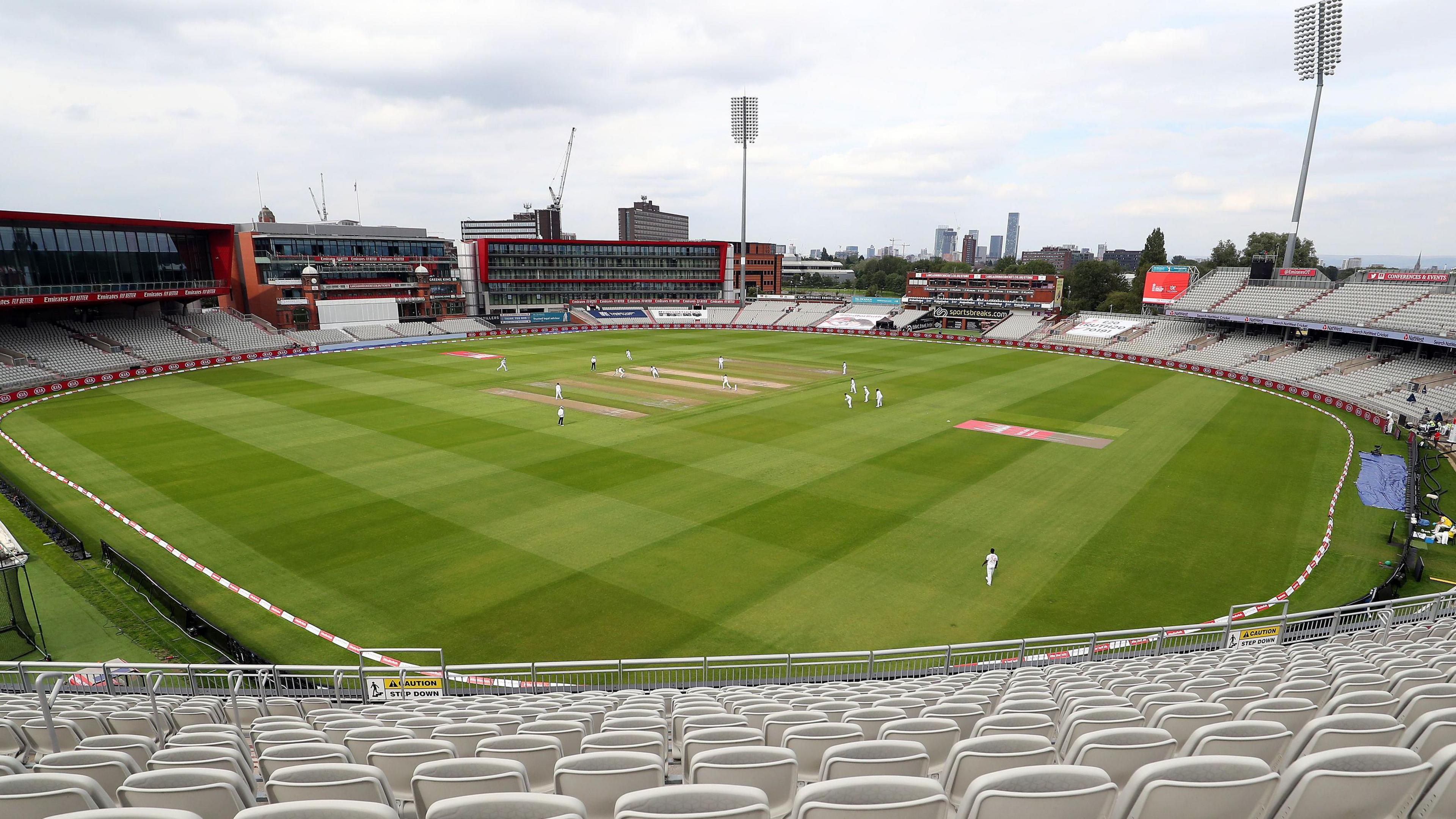 General view of the action on the pitch at Emirates Old Trafford ground in front of empty stands with floodlights the city skyline in the background.