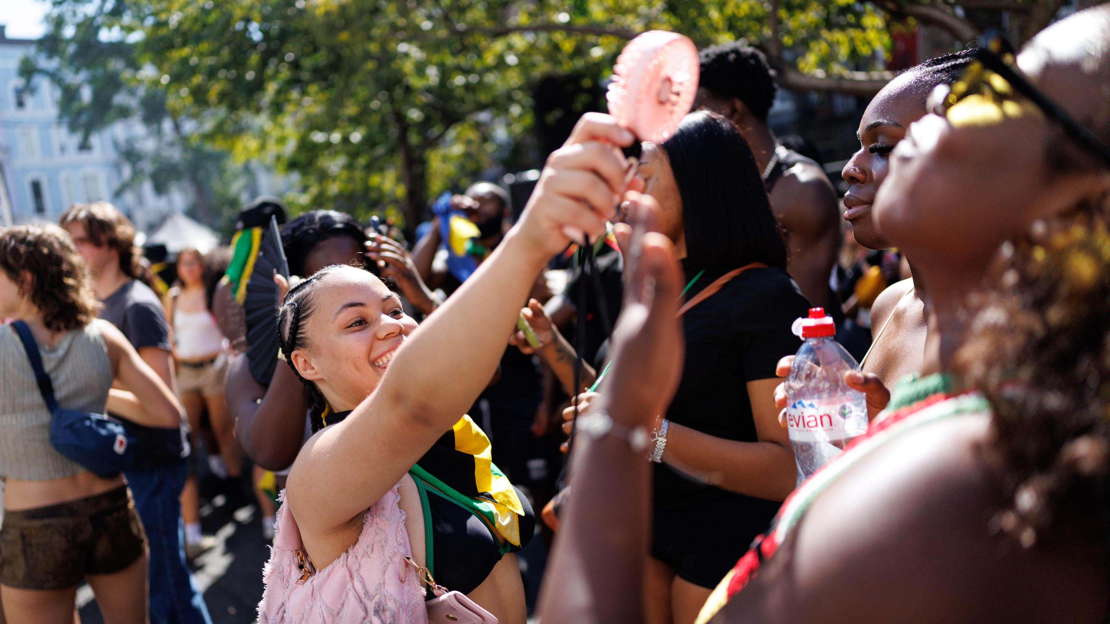 A woman holds a battery powered fan towards another two women in a crowded street.