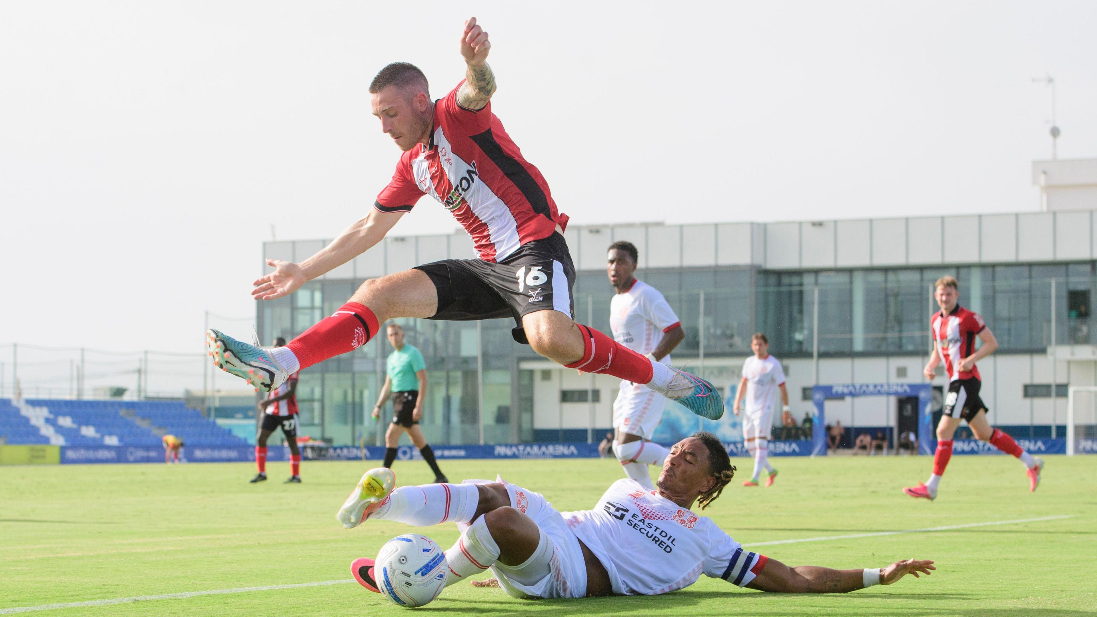 Lincoln City's Dom Jefferies jumps past Leyton Orient's Sean Clare as the latter puts in a tackle during their pre-season friendly in Spain on Friday.