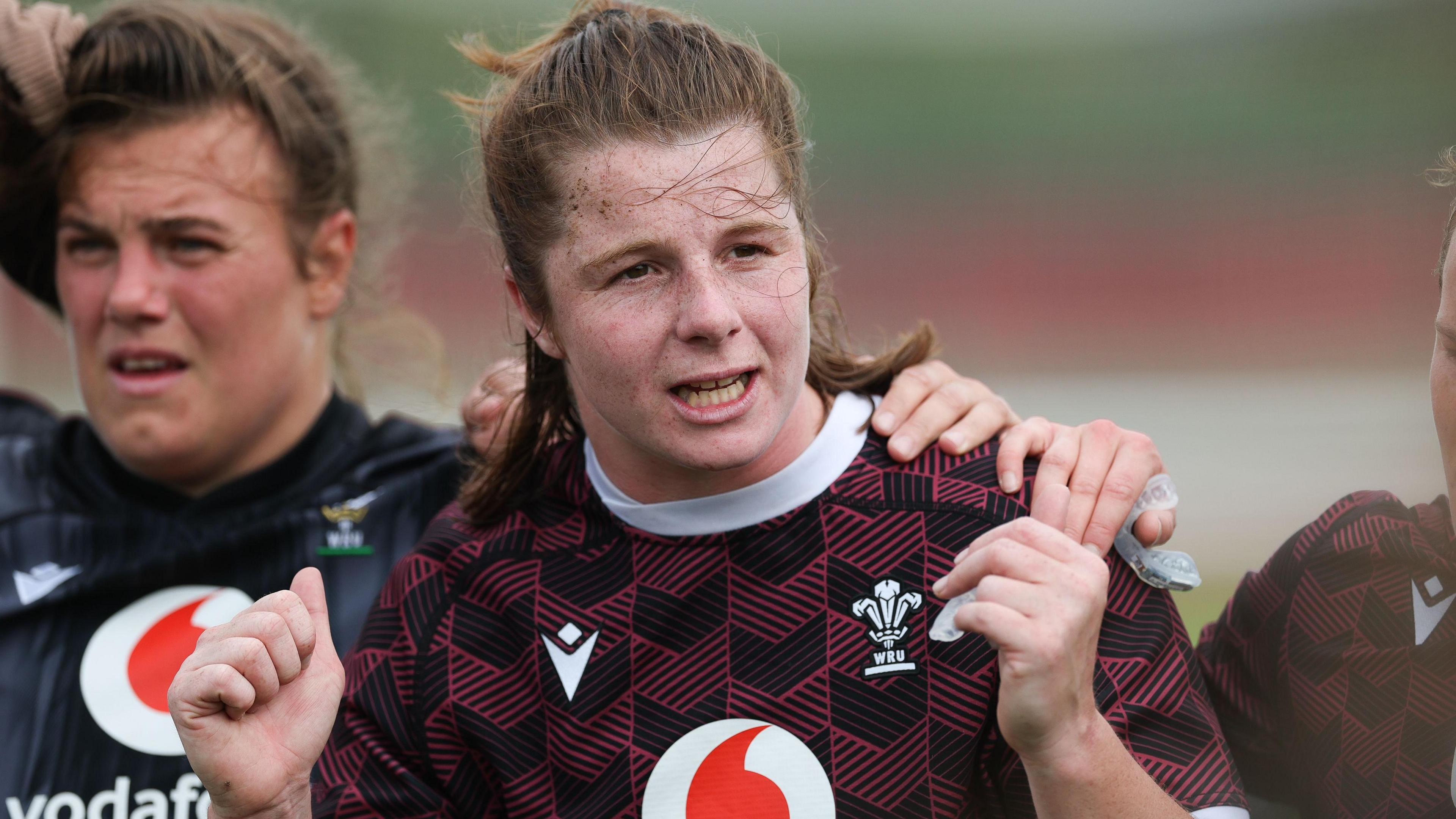 Kate Williams in a Welsh rugby training top offers instructions during a session. Her hands are raised as she makes a point. Carys Phillips' is to her right with her arm over Williams' shoulder.