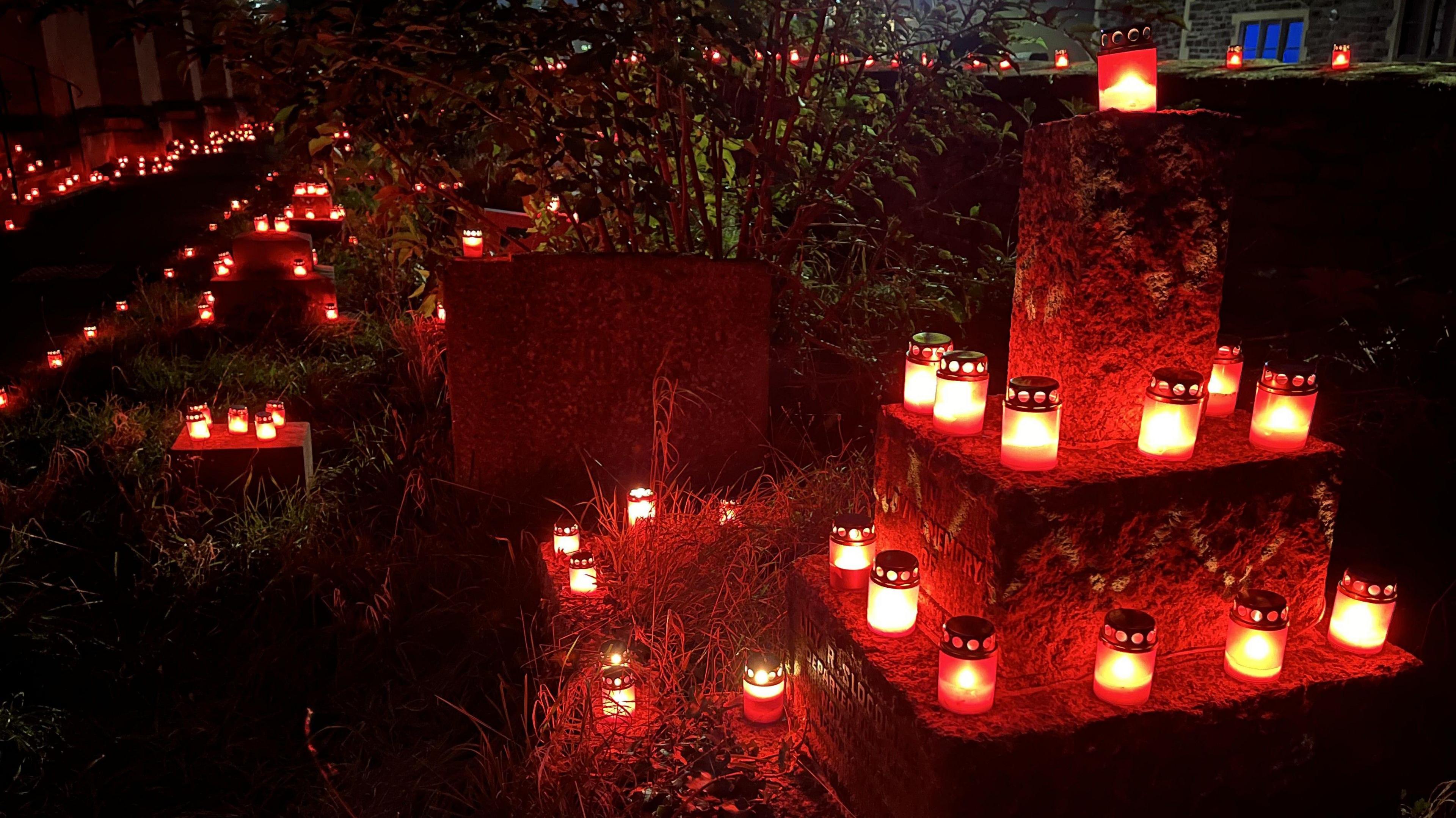 Hundreds of candles inside red containers are seen glowing in the dark in St Paul's Church churchyard in Southville. It is after dark and some of the candles are placed on graves