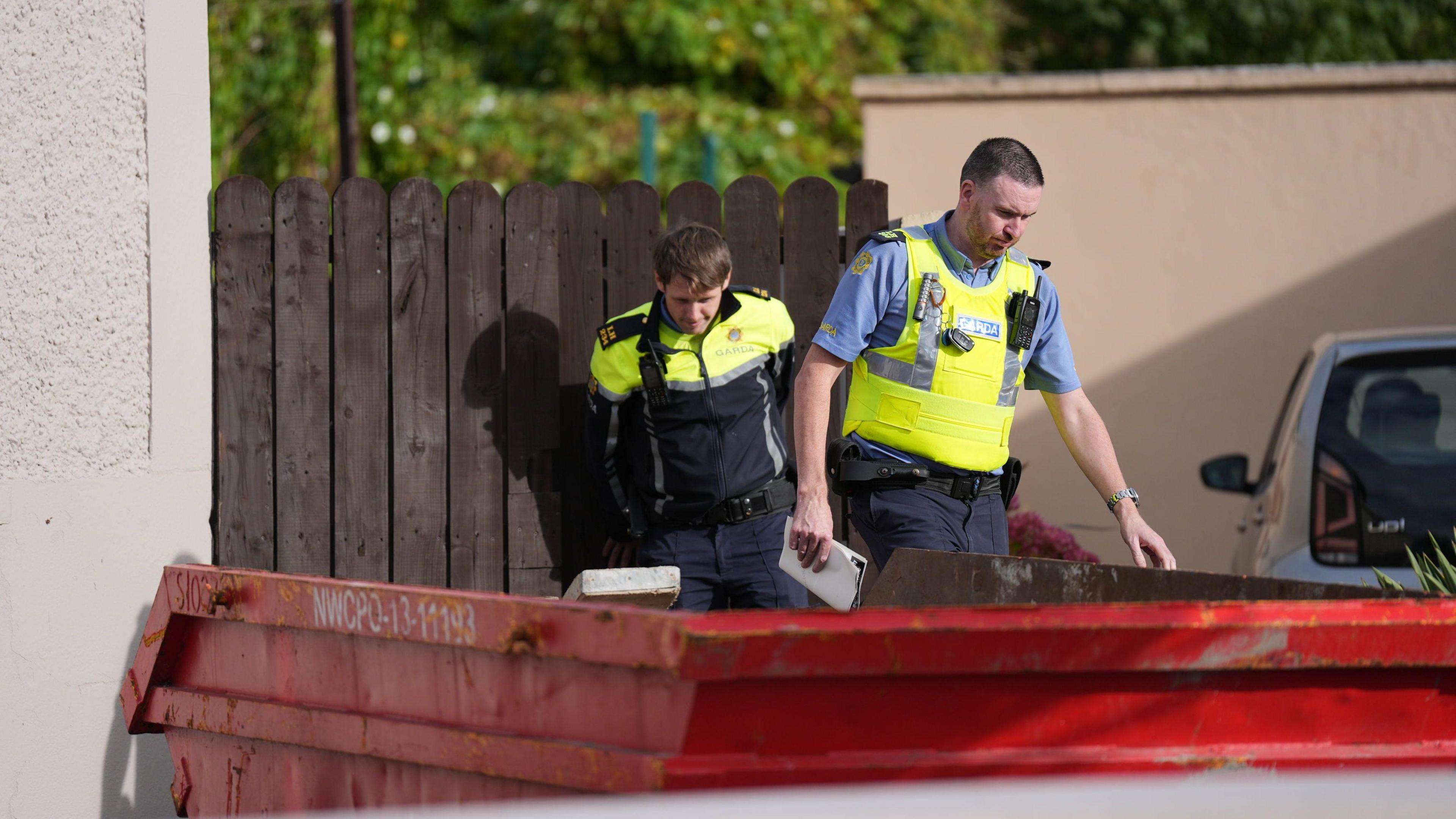 Two uniformed male garda officers on duty during the search for Kyran Durnin in Dundalk. A red metal skip is pictured in foreground.