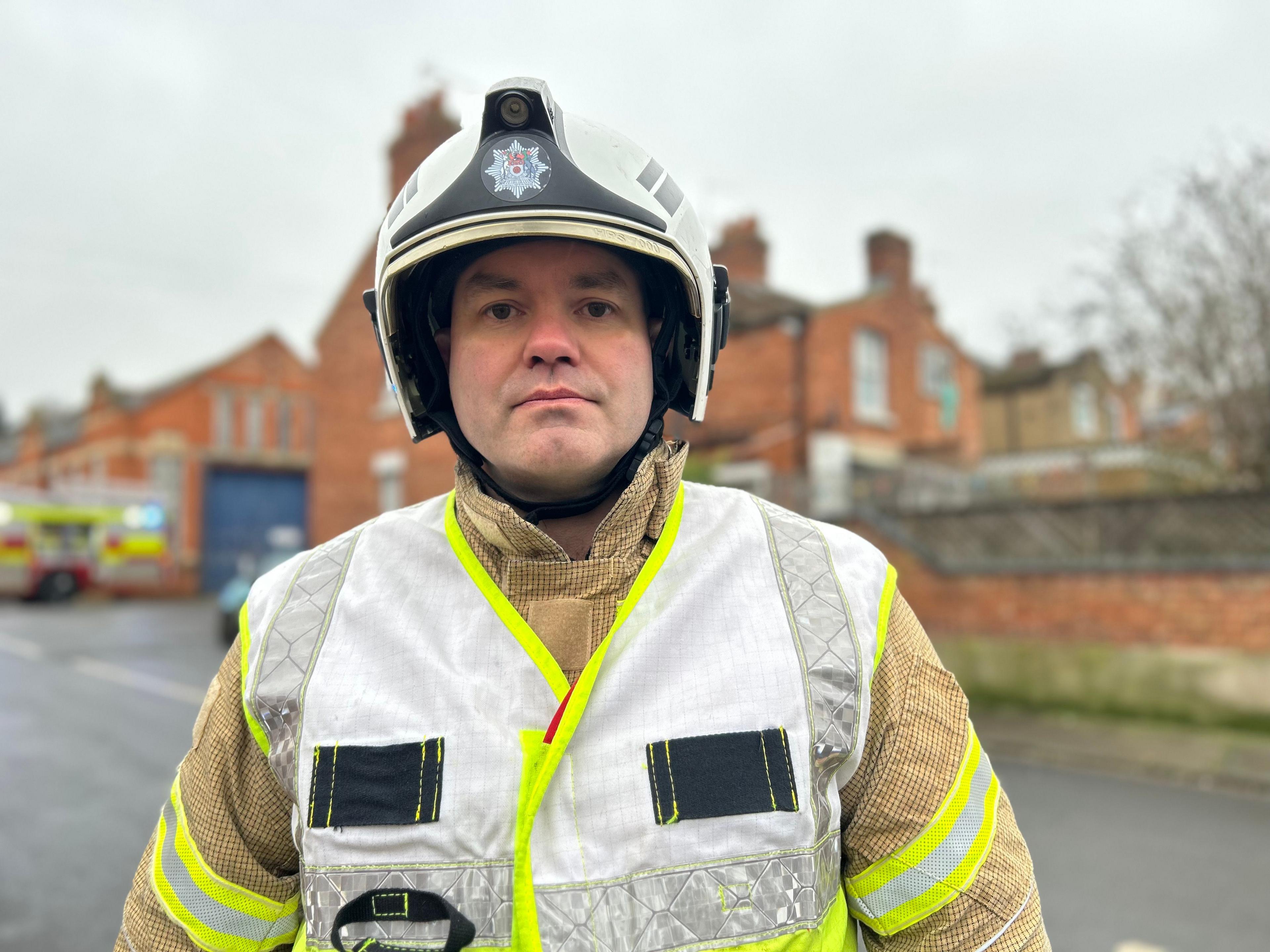 Dan Retter wearing a white helmet with the service insignia and a fire protection jacket and high visibility vest, standing on a street.