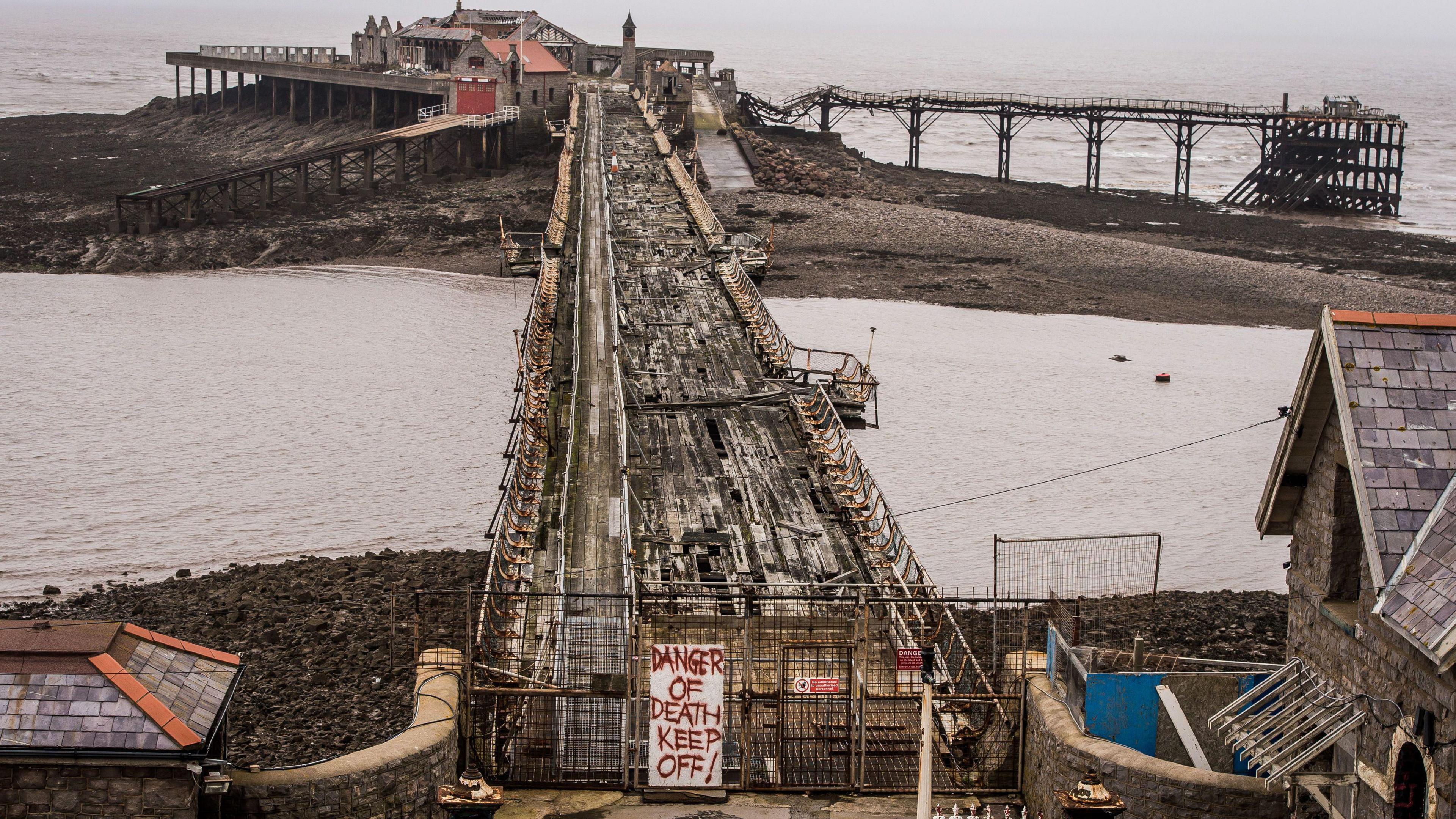 A photo of the derelict pier, with a sign reading "danger of death, keep off!" in the foreground