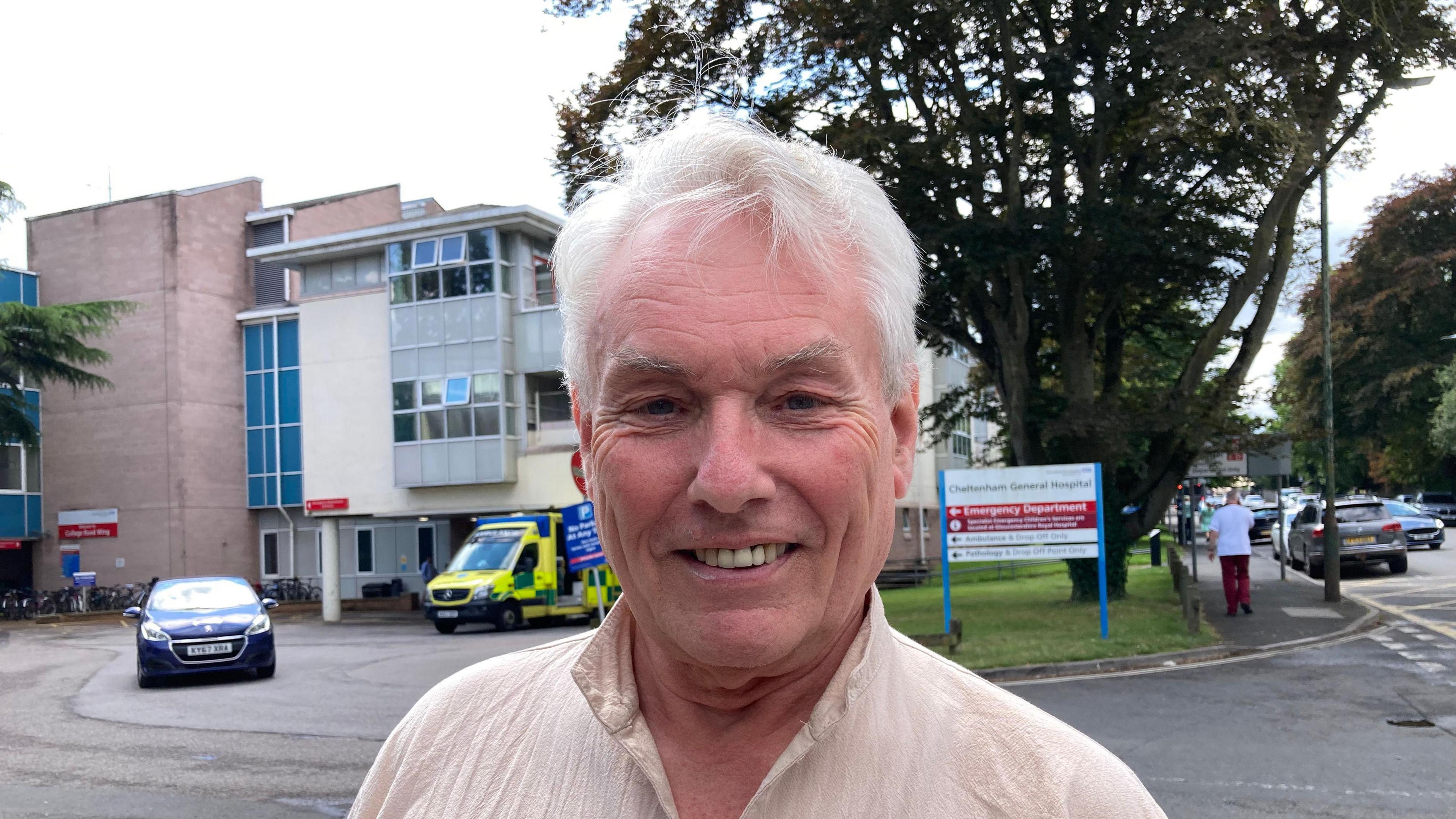 Julius Marstrand smiling as he stands outside of Cheltenham General Hospital, with ambulance and cars in the background.