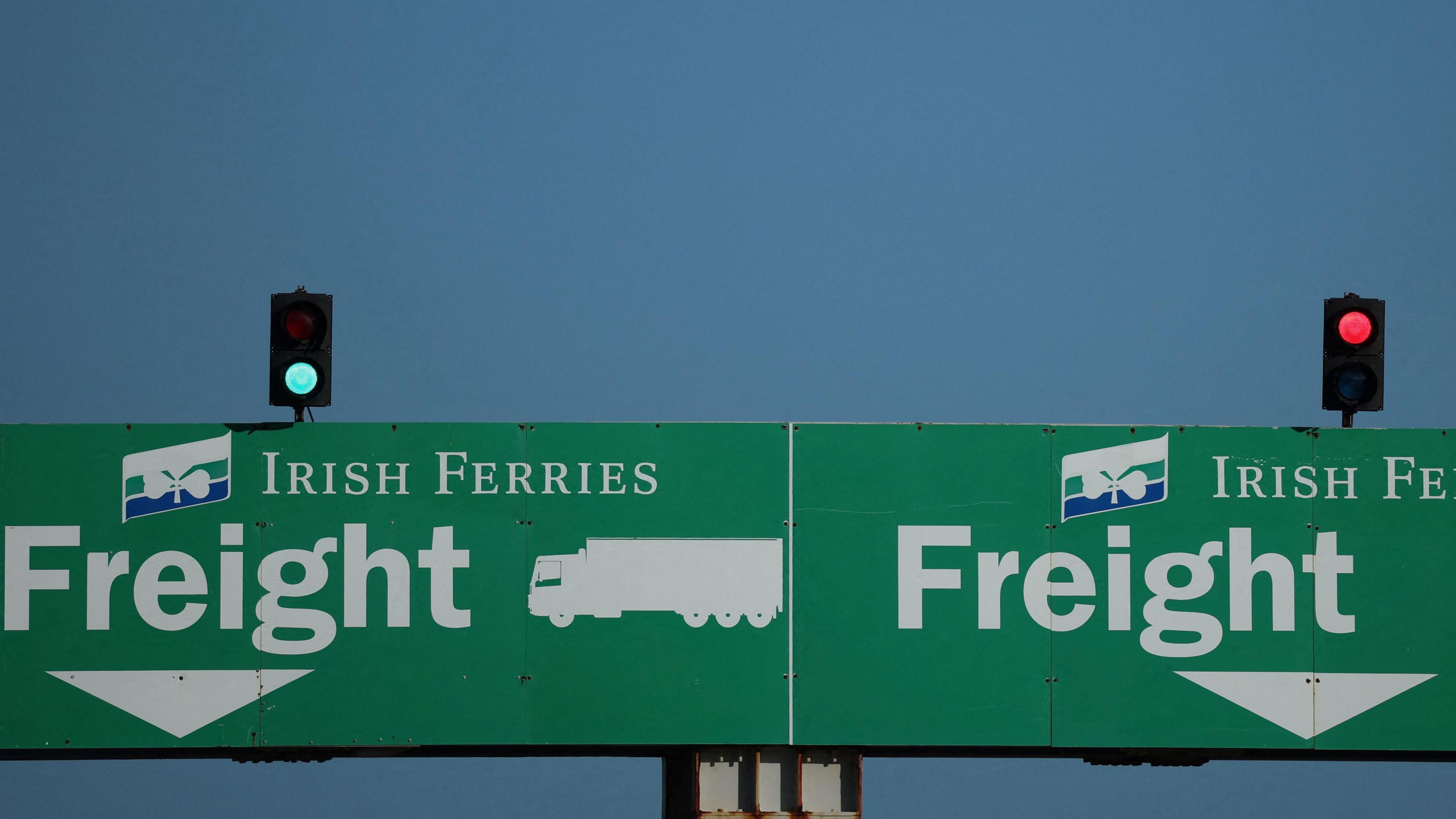 Two green signs. Both signs have the words 'Irish Ferries Freight' written on them. Above each sign is a traffic light. The traffic light on the left is green, while the traffic light on the right is red. 