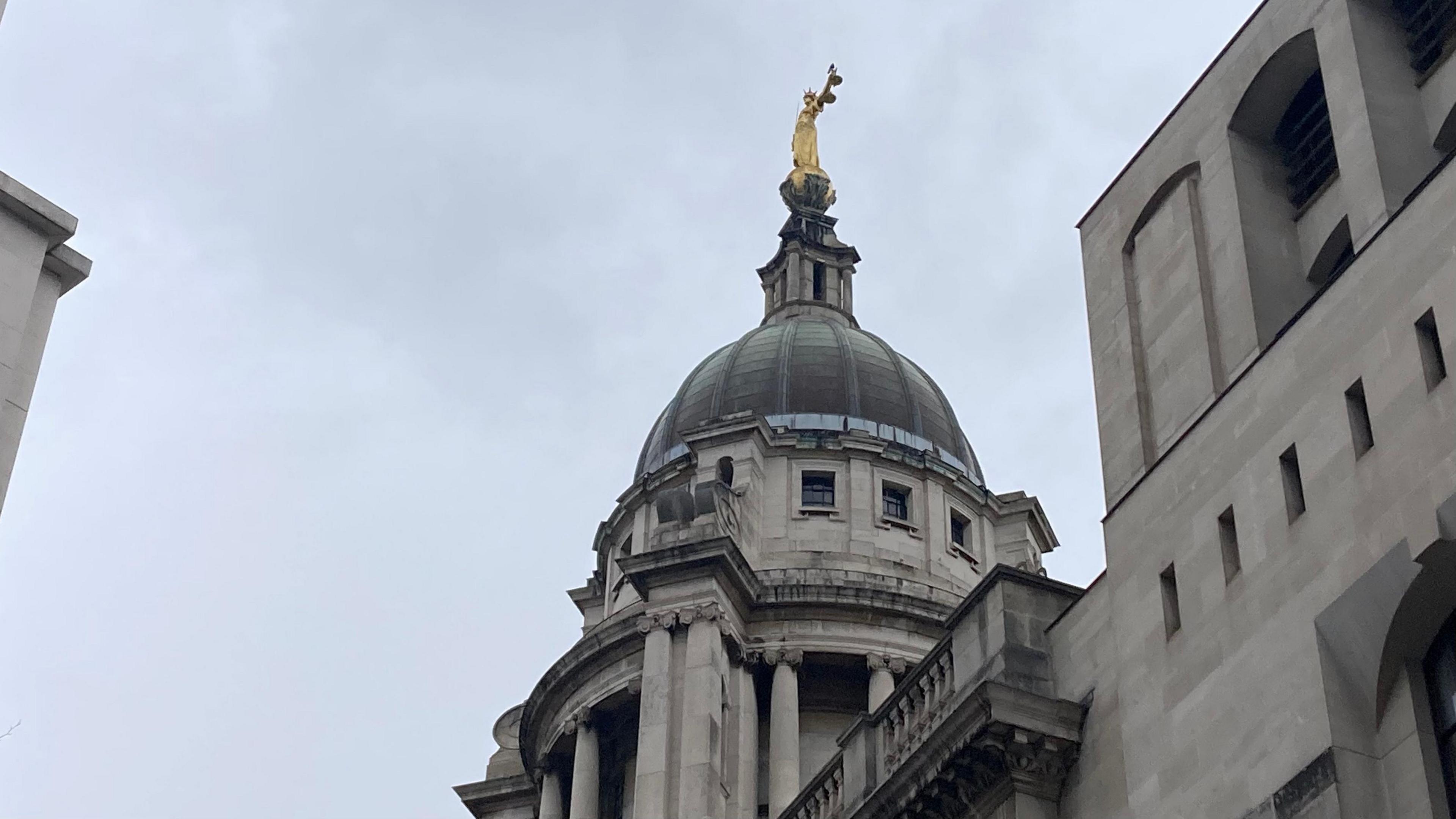 The top part of the Old Bailey in London - a pale grey stone building with a dome and golden statue on top. 