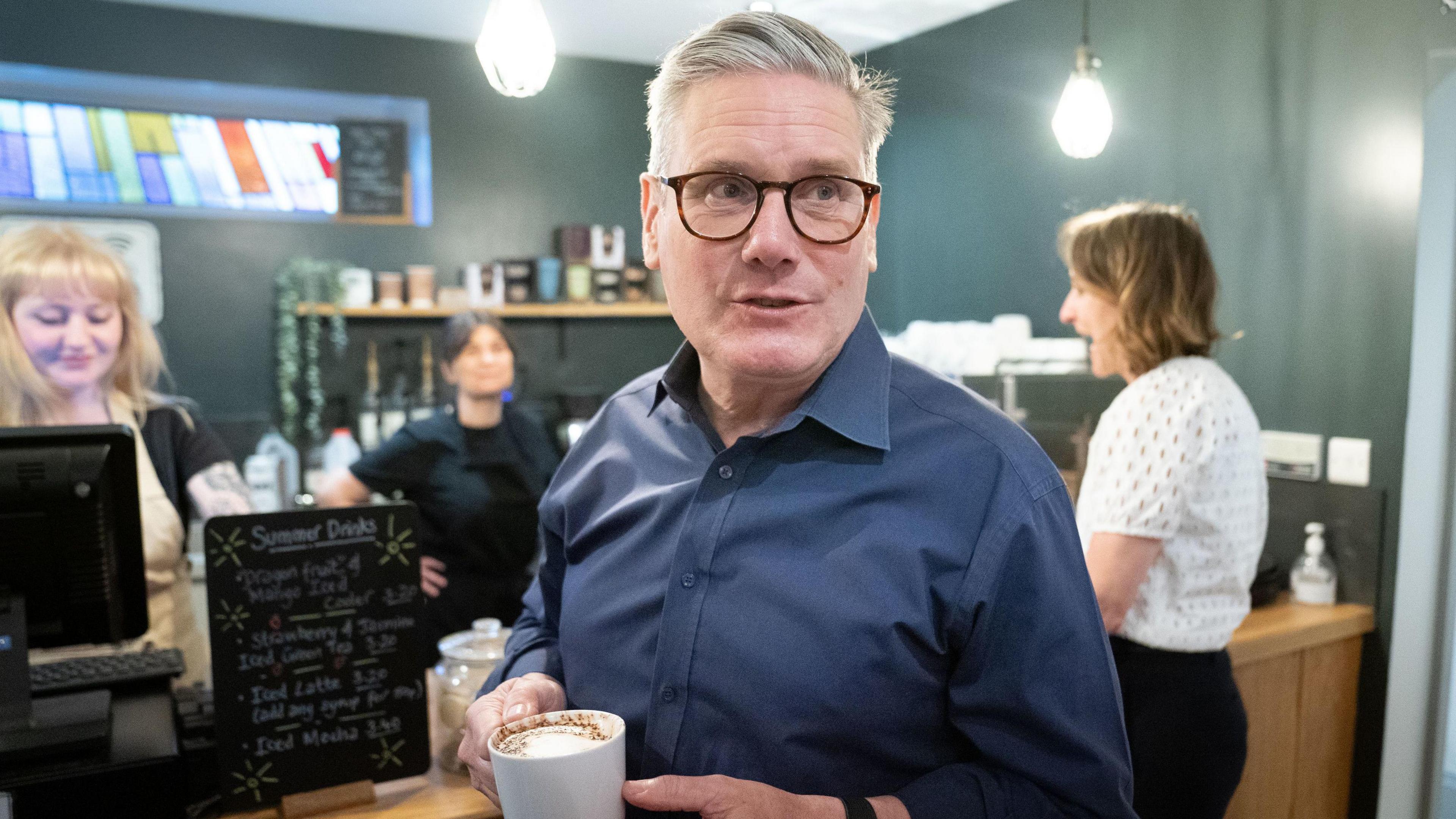 Keir Starmer holds a cup of coffee and faces the camera in a cafe on the election campaign trail