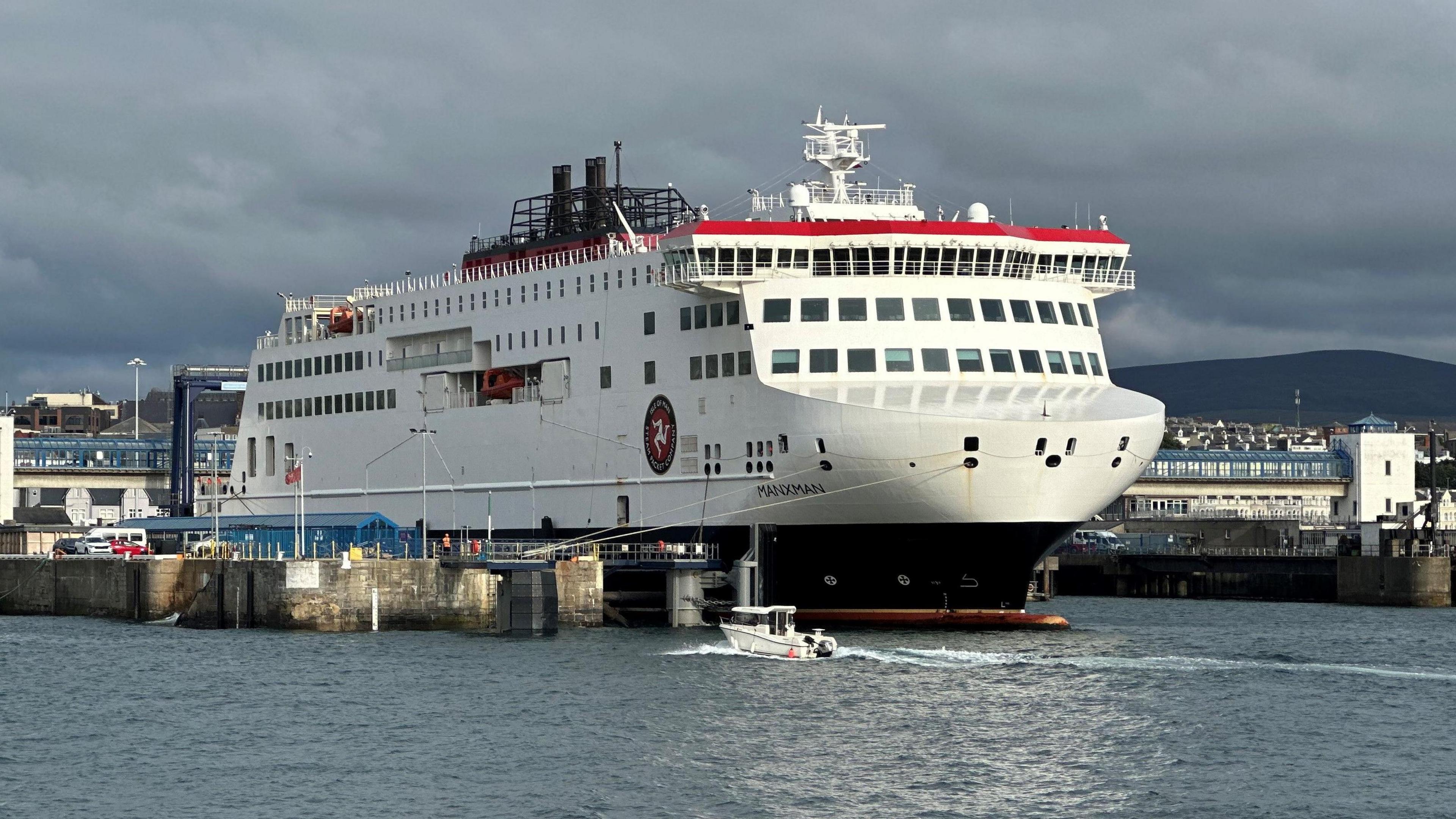The Manxman ferry moored in Douglas Harbour. It is in the Steam Packet colours of red white and black and has the company's logo of a three-legs-of-Mann on this side.