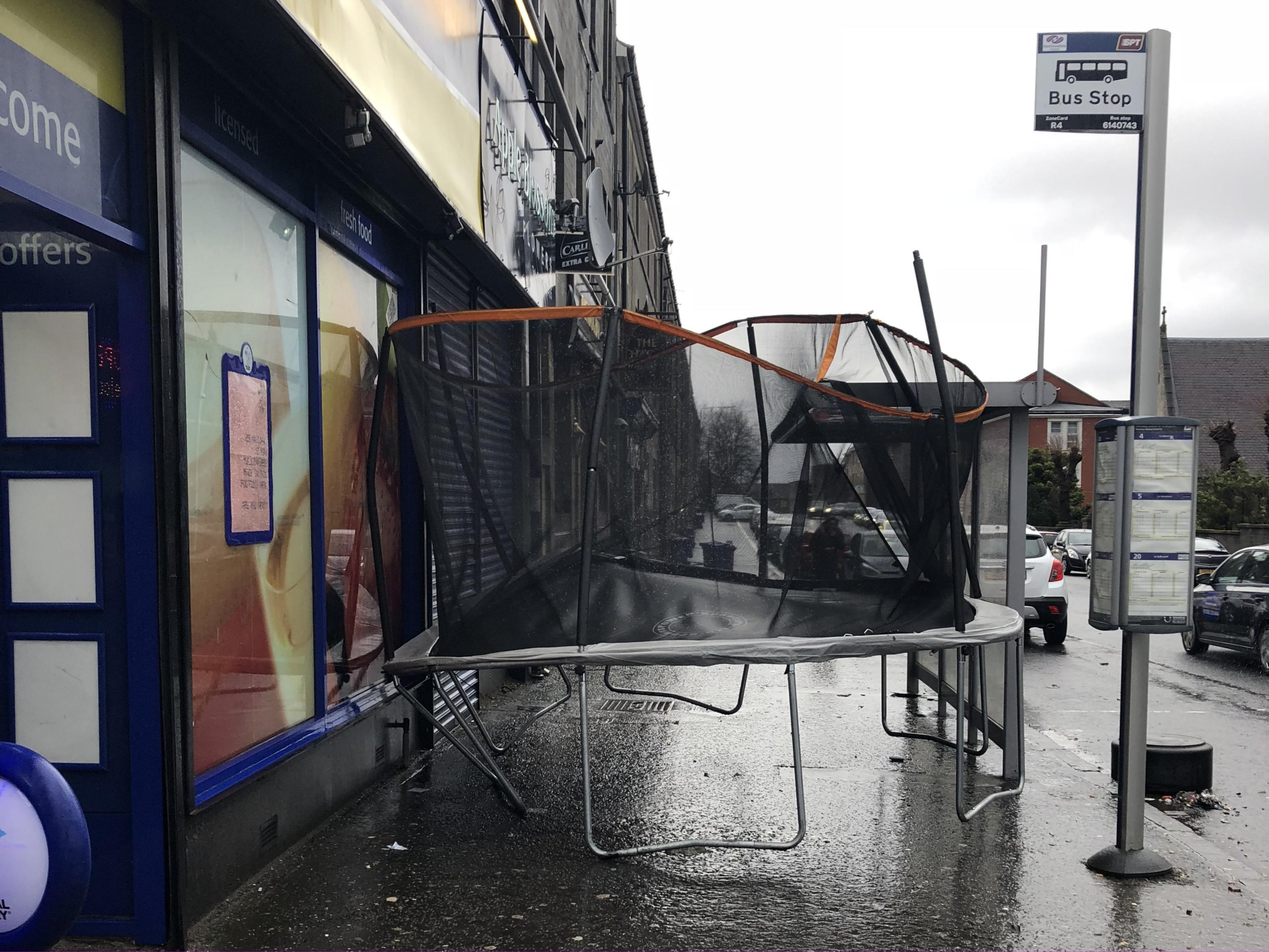 A trampoline stuck between a shop and a bus stop.