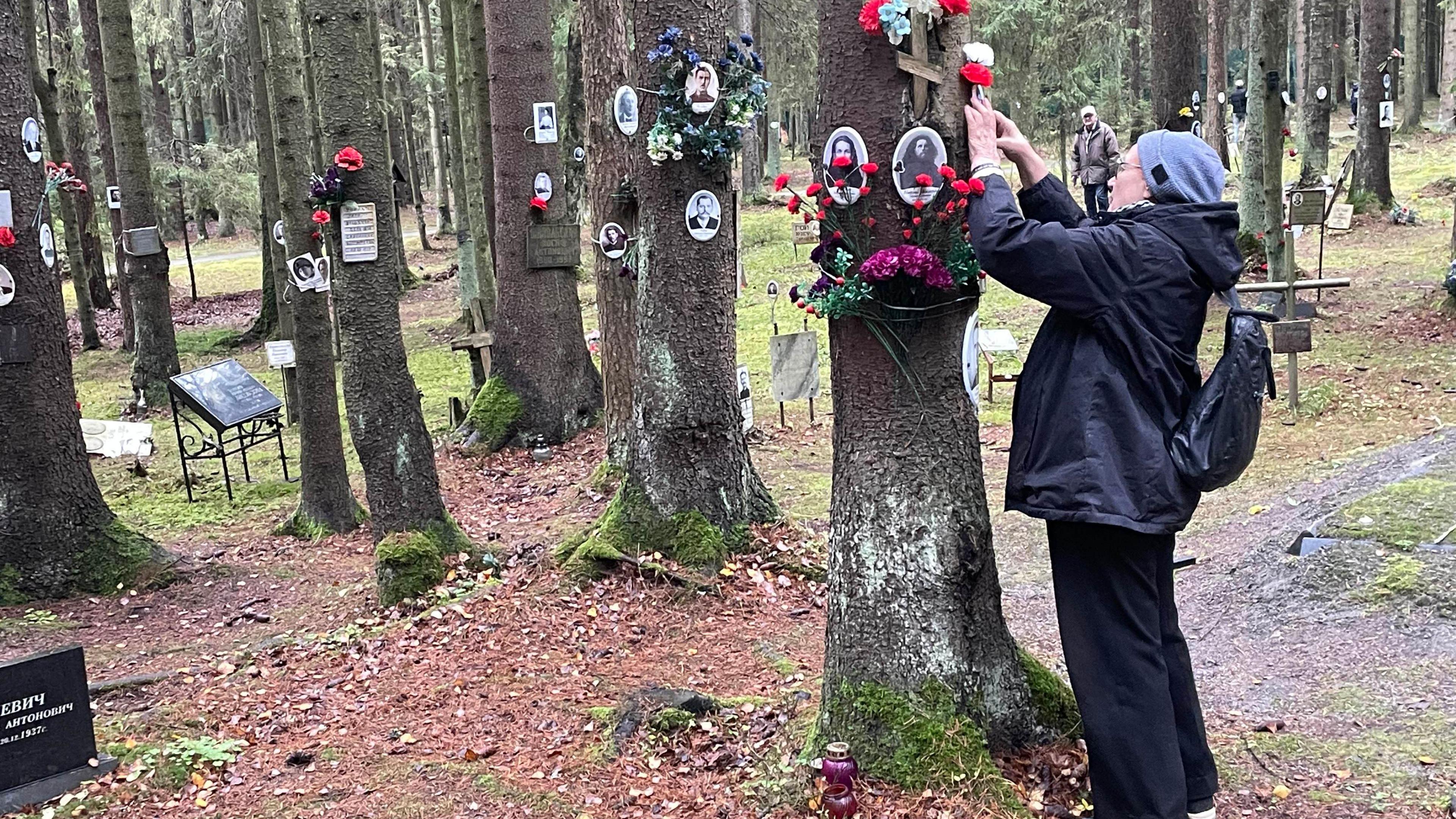 A woman puts flowers on a tree in the woods outside St Petersburg where tens of thousands of Stalin's victims are buried