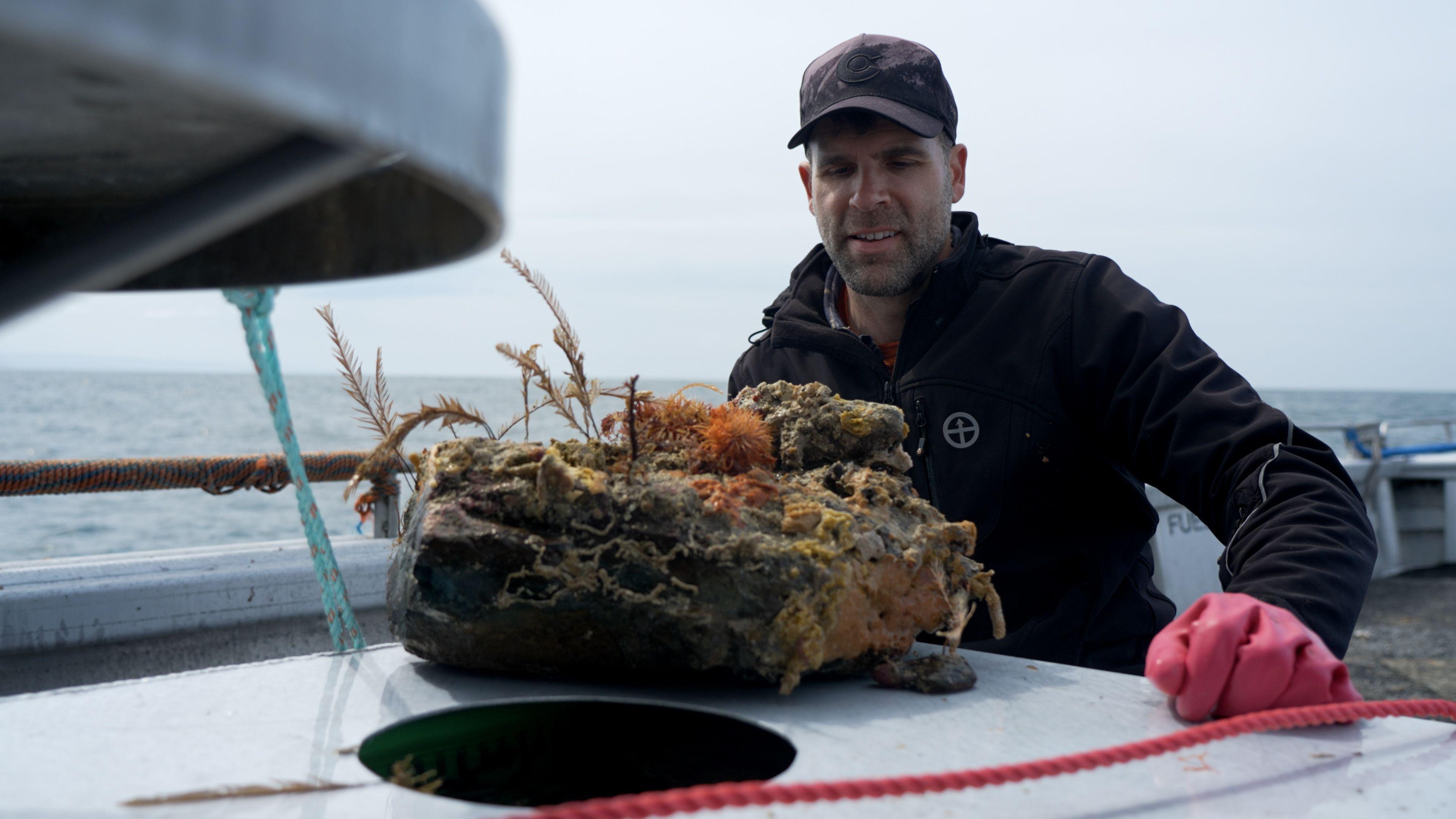 dr Chris with a rock covered in marine life on a boat