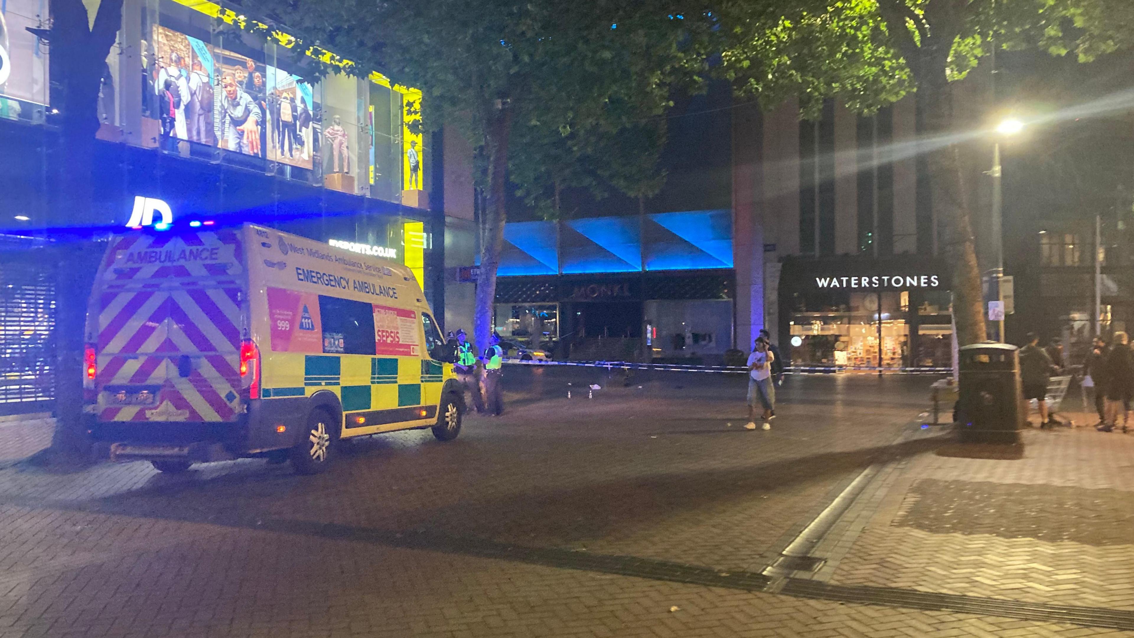 A different angle of the police cordon, with an ambulance in the foreground parked in front of JD Sports