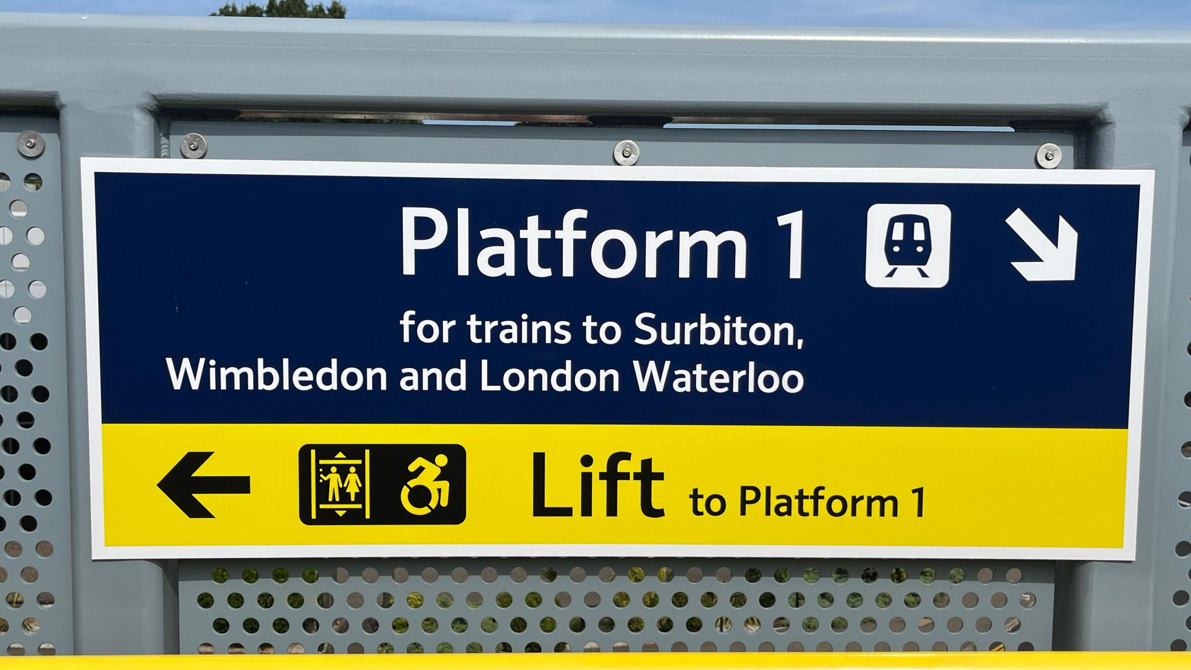 A sign pointing to Platform 1 for trains to Surbition, Wimbledon and London to the right and pointing to the left for the lift