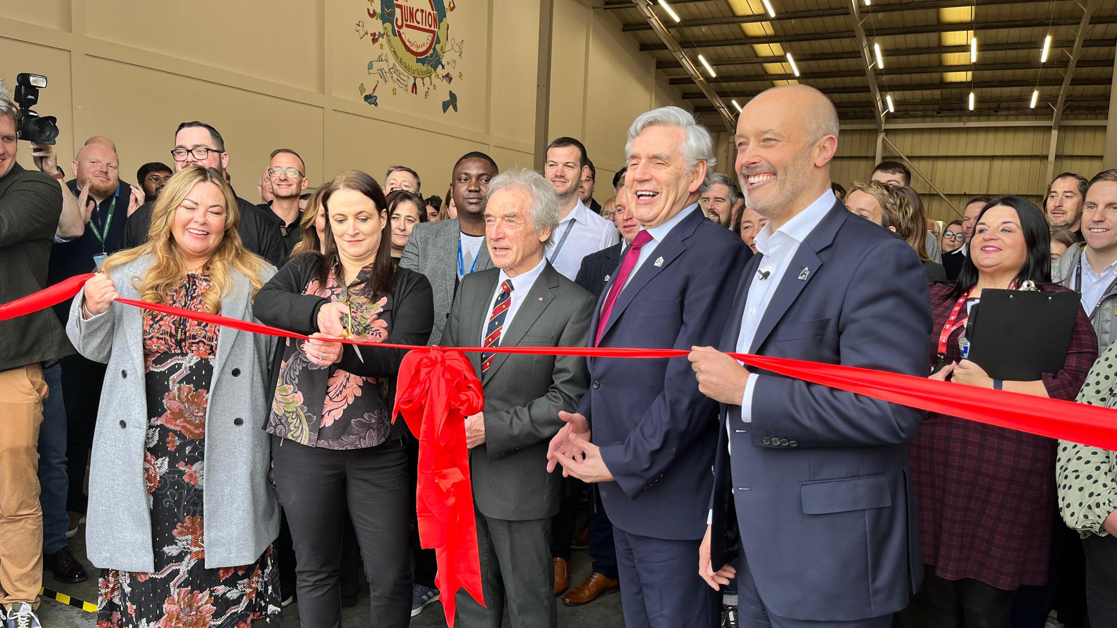 The Junction's Beth Major cuts the ribbon and officially opens the Multibank centre in Middlesbrough on Tuesday. She is surrounded by people wearing smart clothes, including Gordon Brown.