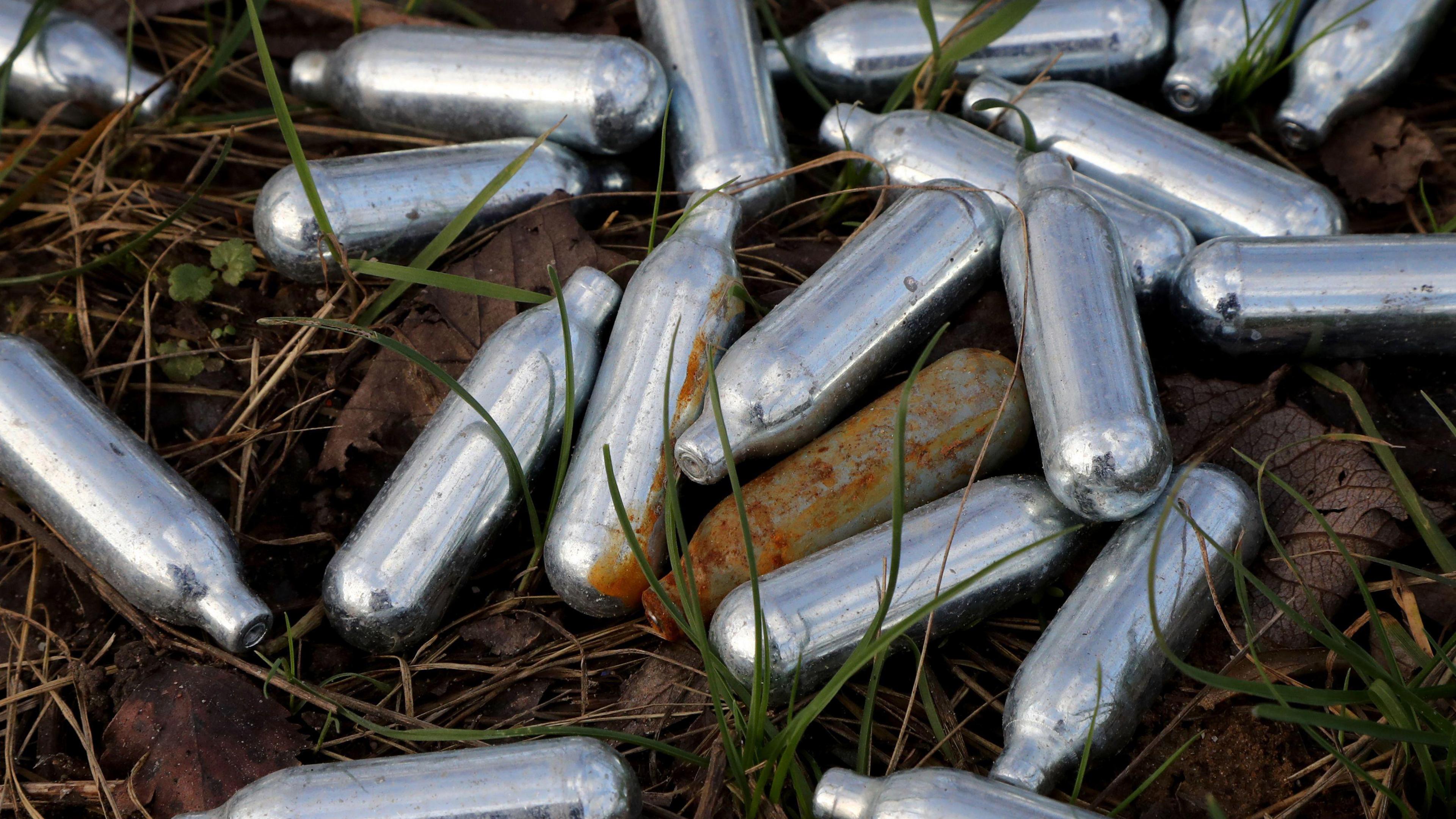 A pile of small, silver-coloured canisters abandoned on grass.