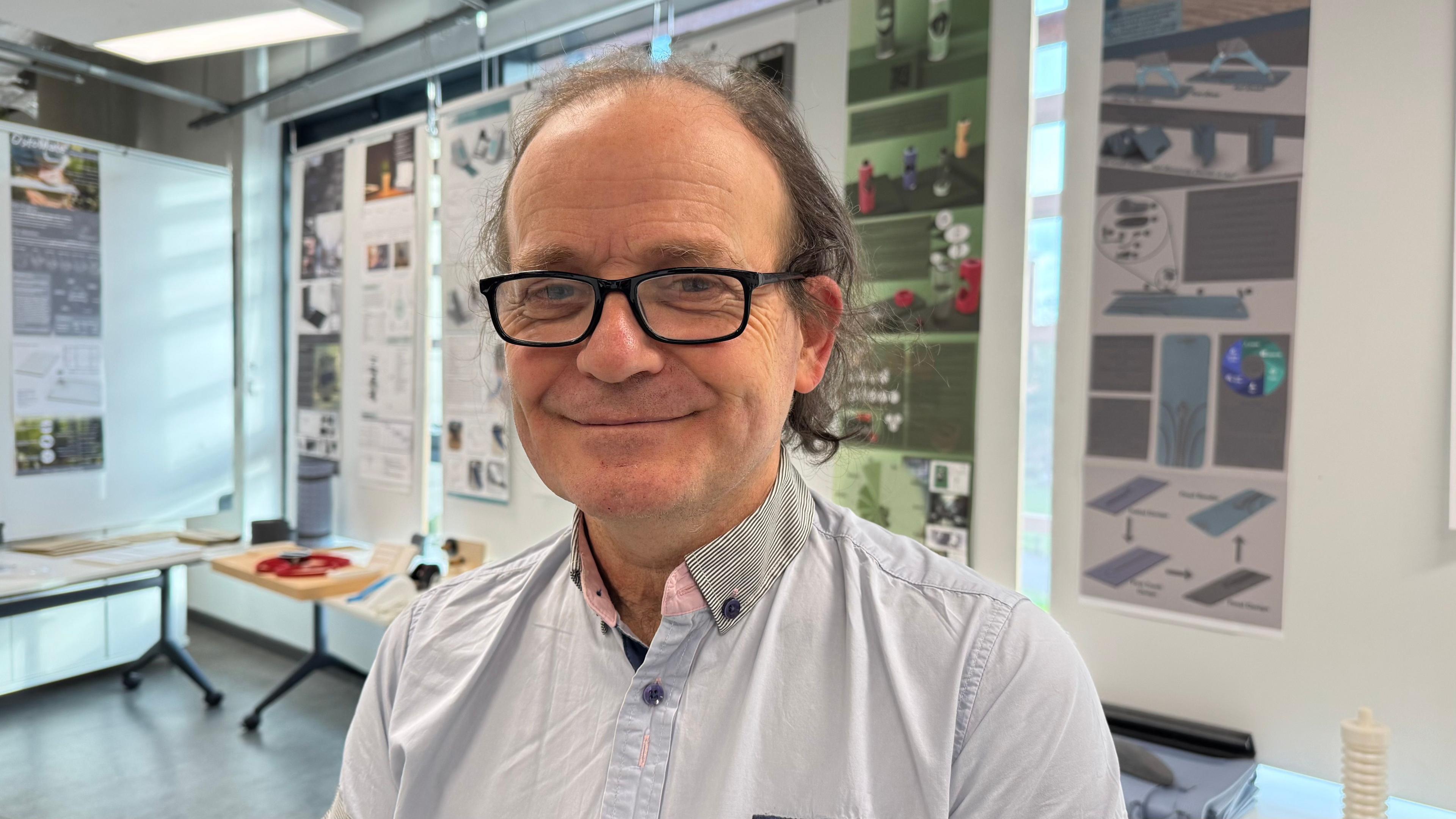 A bespectacled man in a pale blue shirt in the university design lab