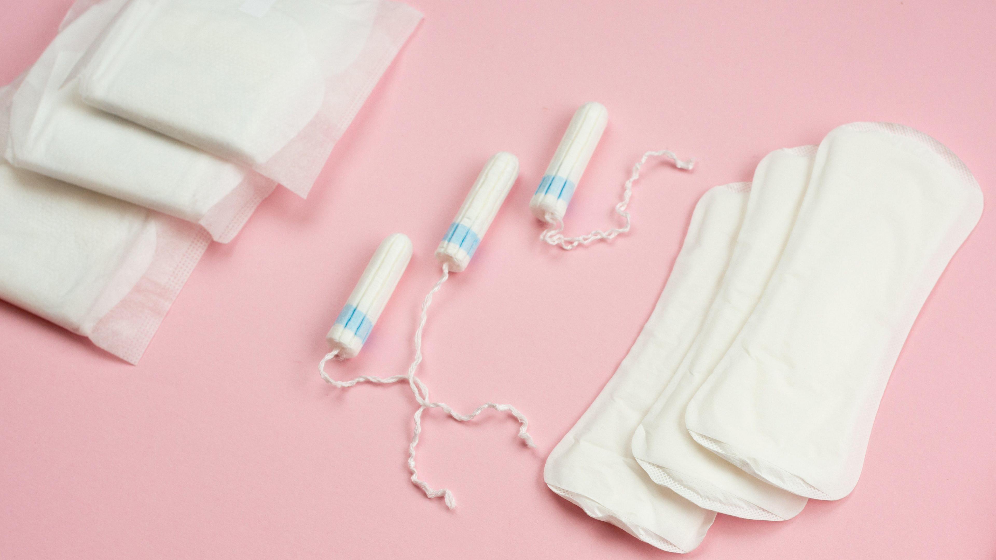 Unused sanitary towels, tampons and panty liners on a pink background.