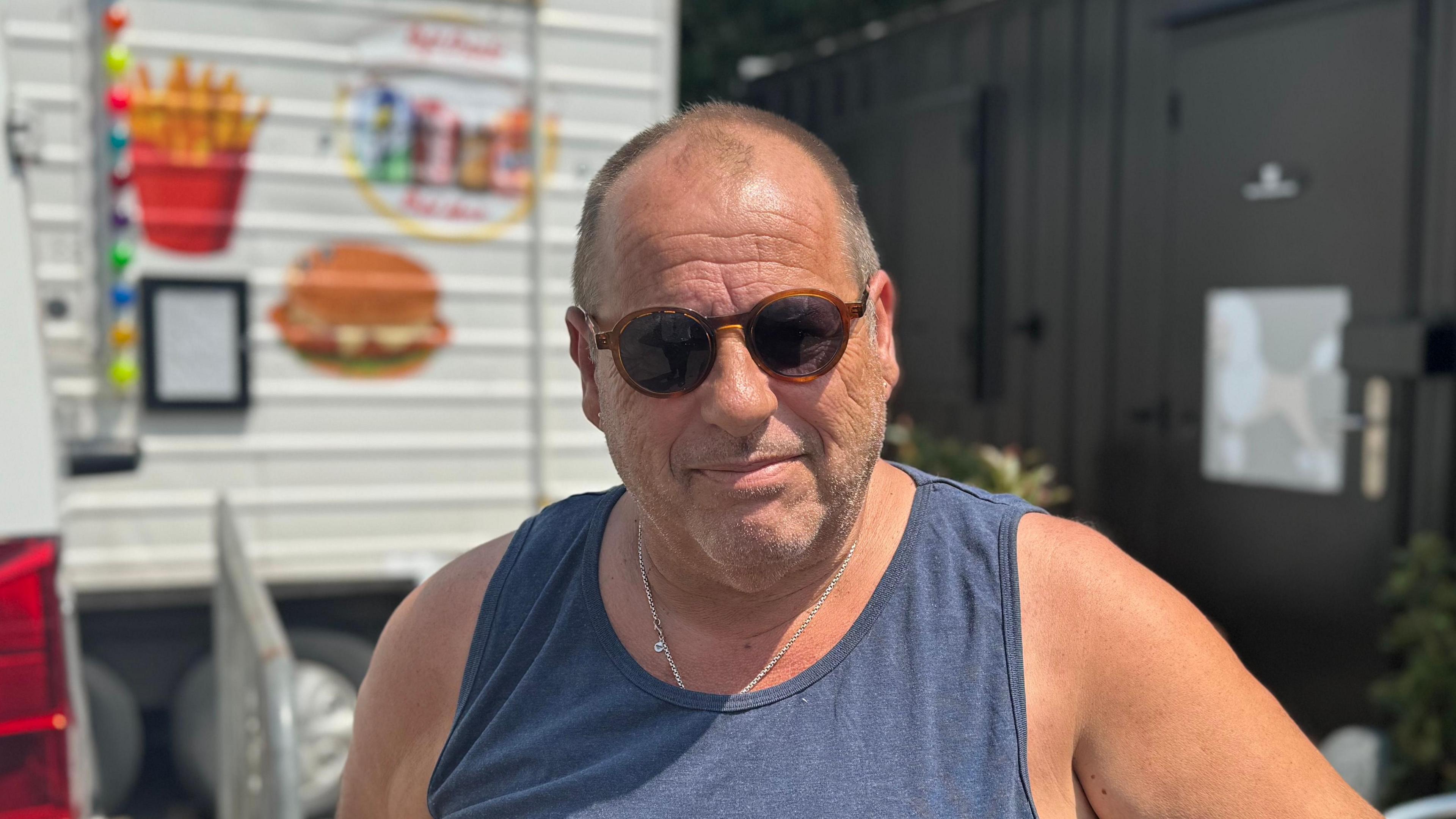 A head and shoulders image of Neil Austin. He is wearing dark sunglasses and a navy blue vest. He is looking directly into the camera.