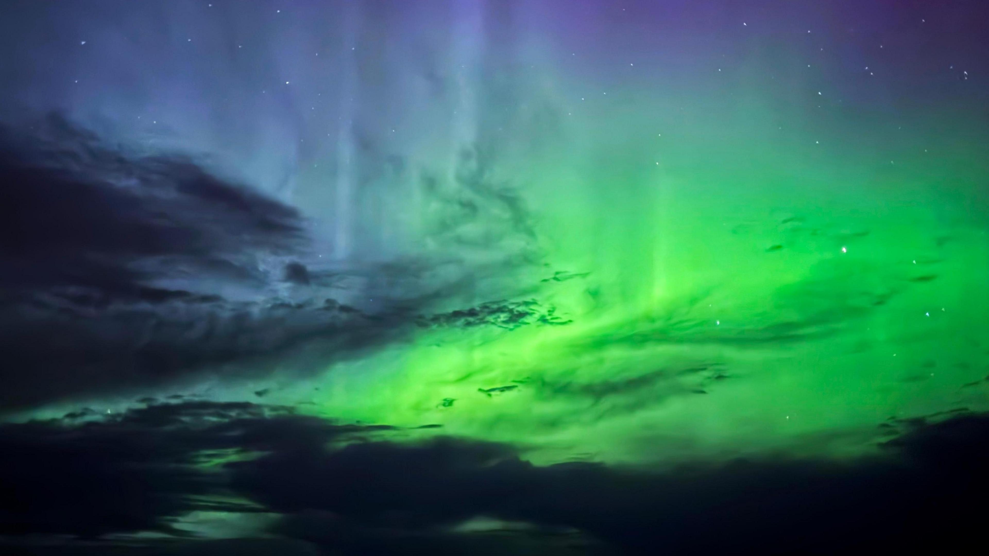 bright green colours of the aurora with some darker shades of cloud covering parts of the night sky.