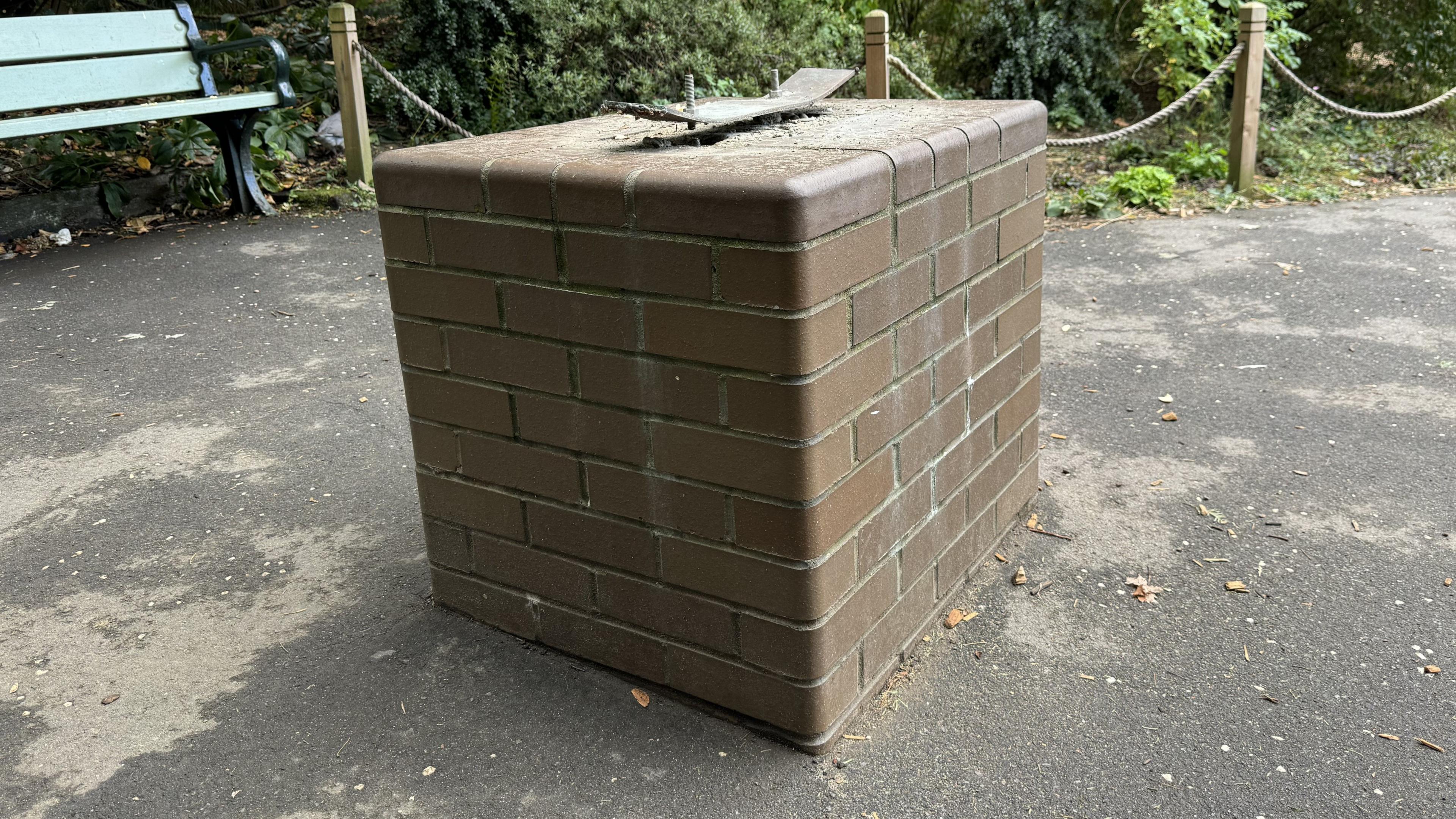 A plinth in a park with two empty screws on top of it