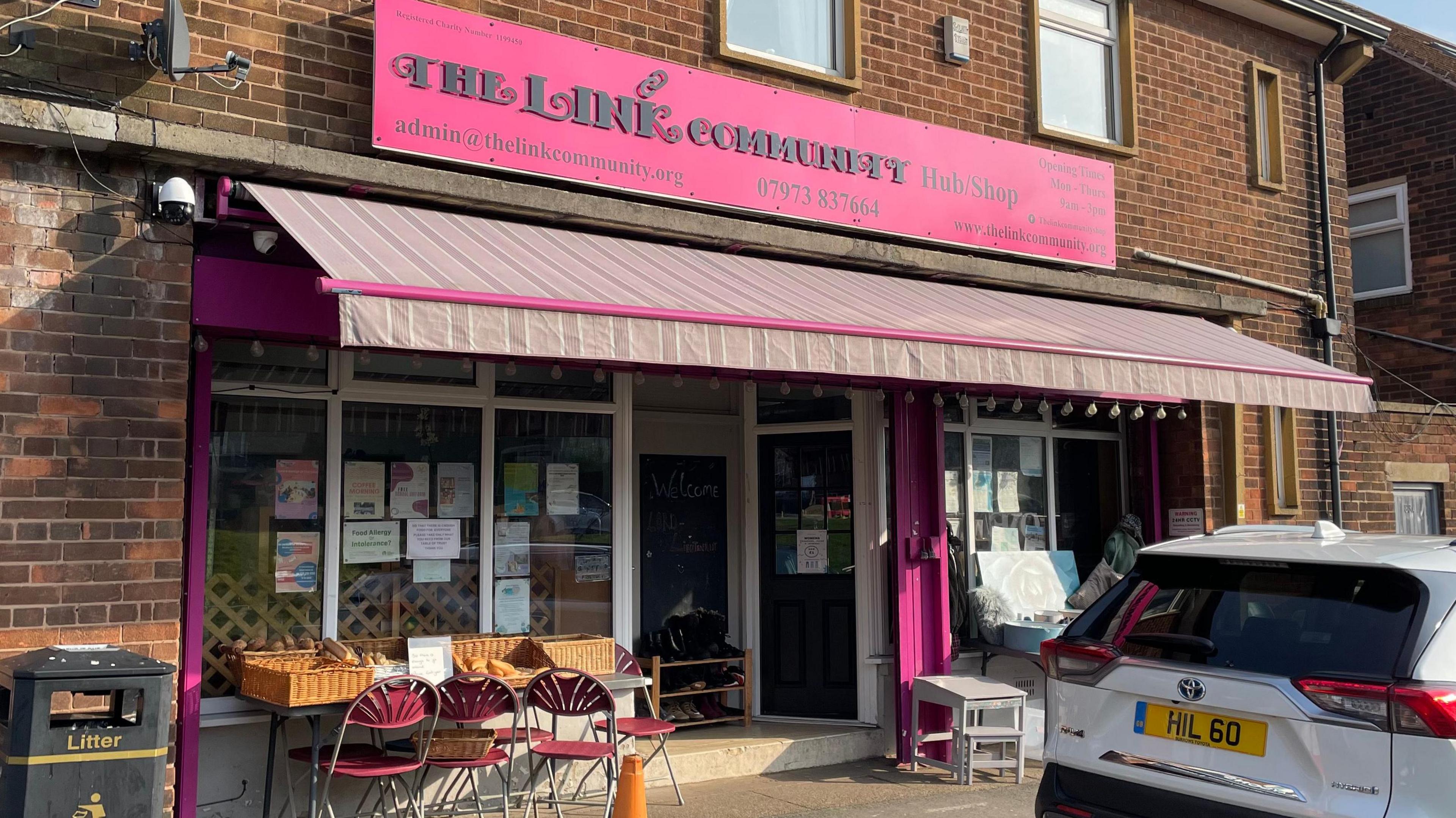 The front of the community hub and second-hand shop, which has a pink sign and canopy.