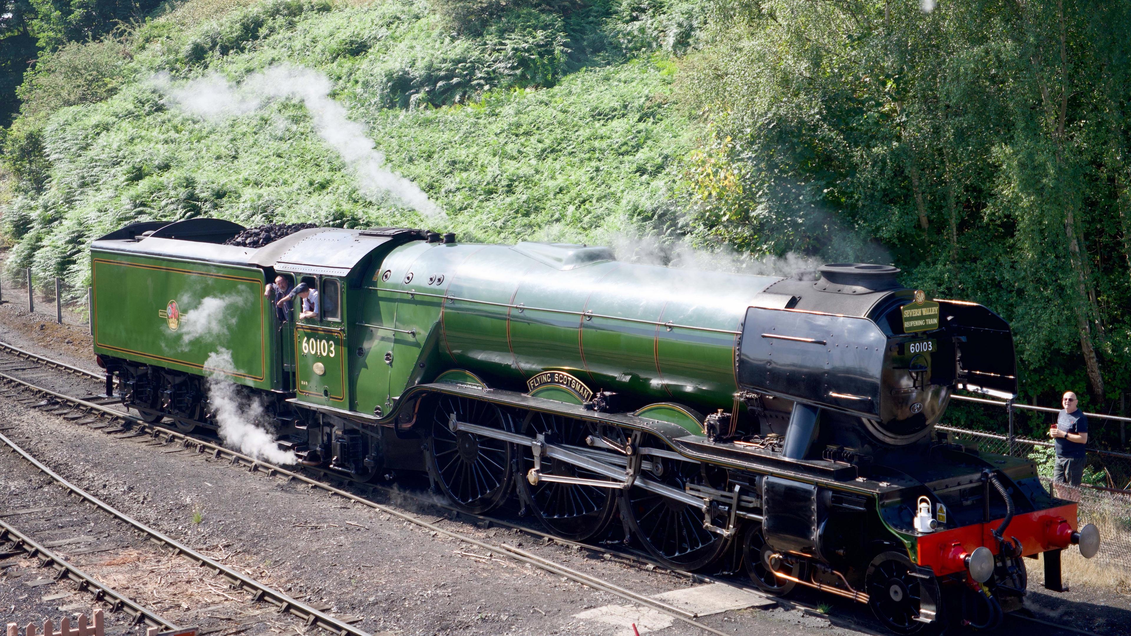 Steam comes out of a green locomotive as it travels along the tracks on a sunny day