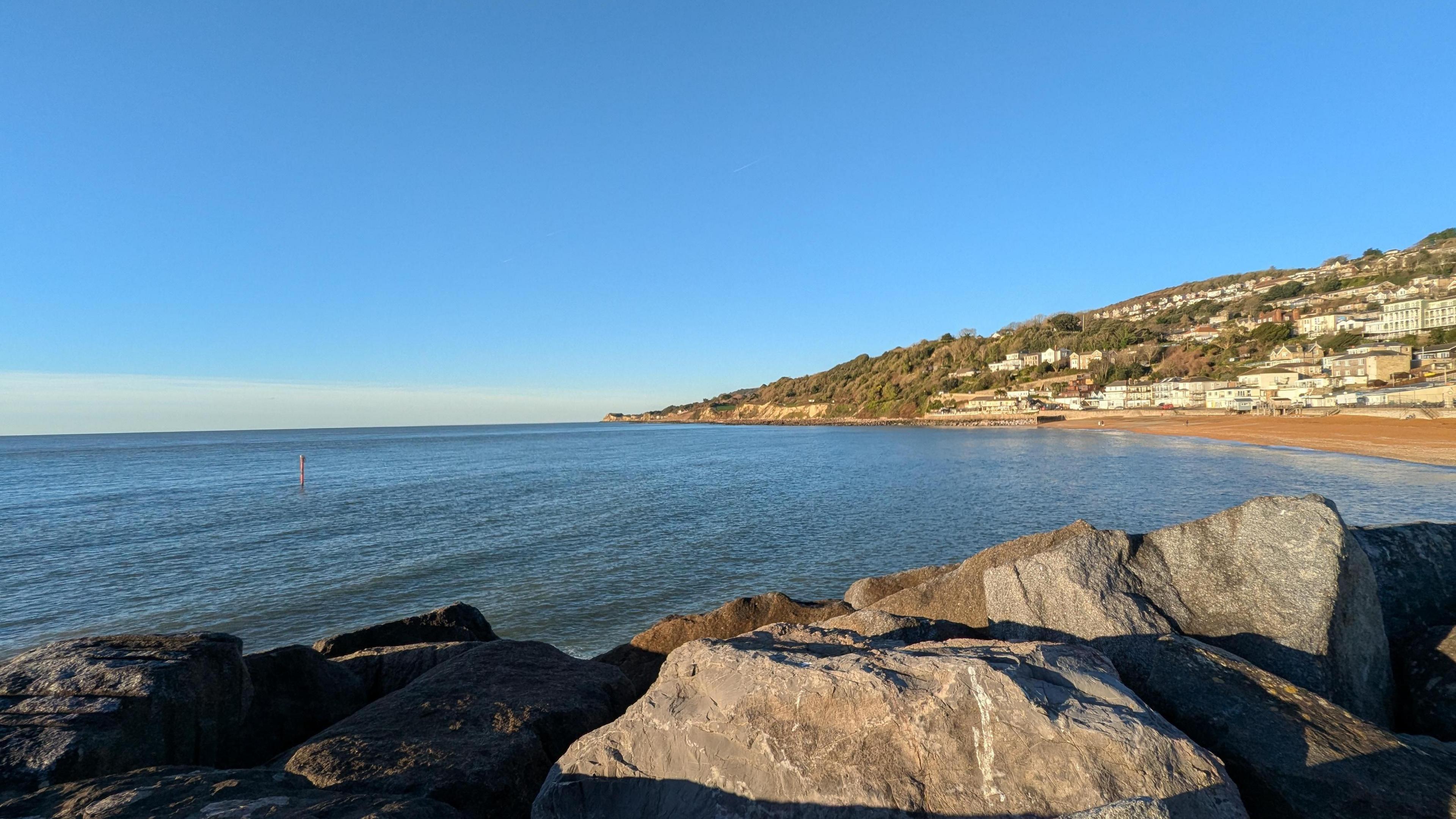 Dark blue, calm seas and bright blue skies taken in Ventnor, Isle of Wight with a big rock in the foreground.