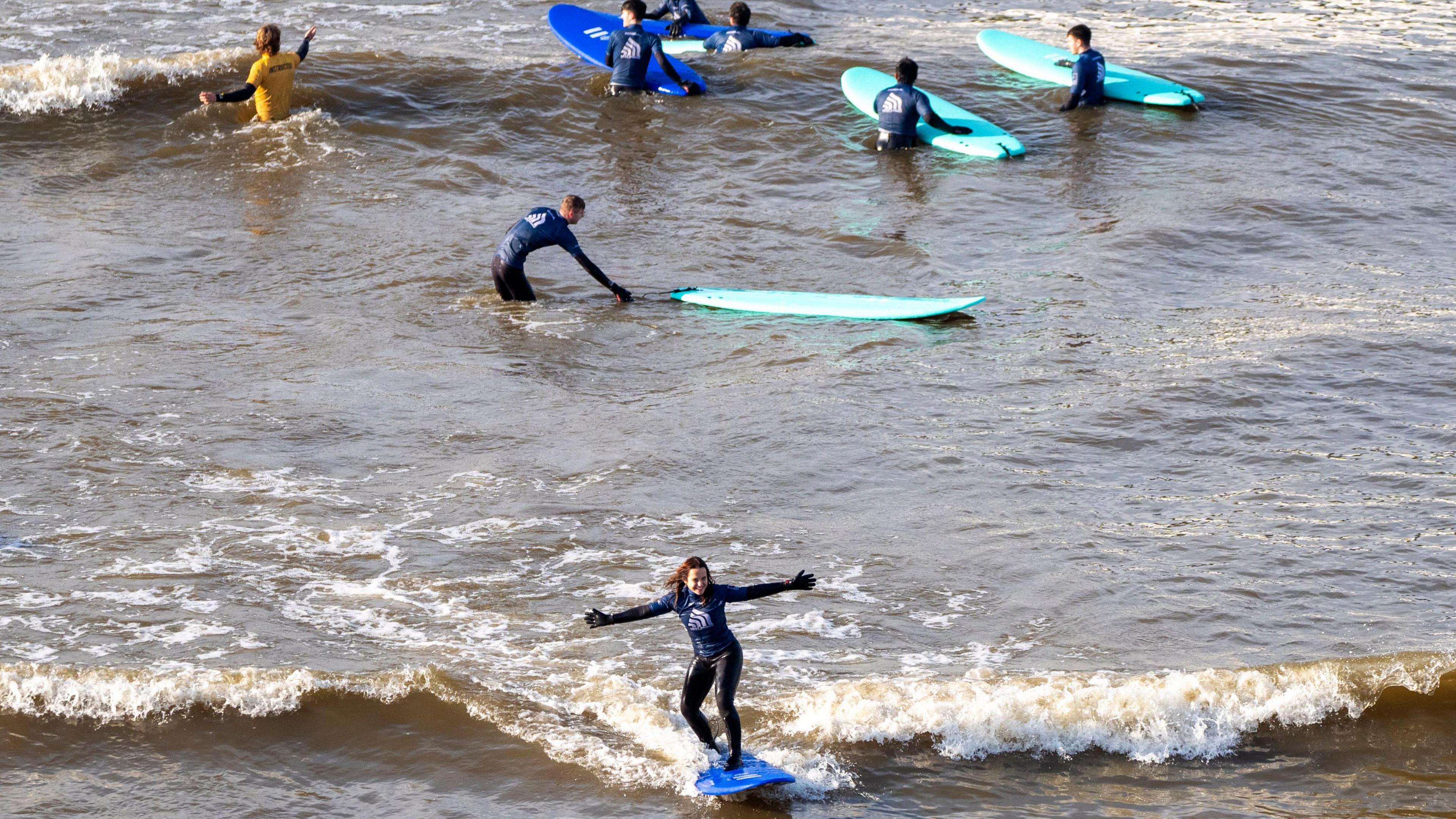 A surfer is riding a wave while others stand in the water with their boards.