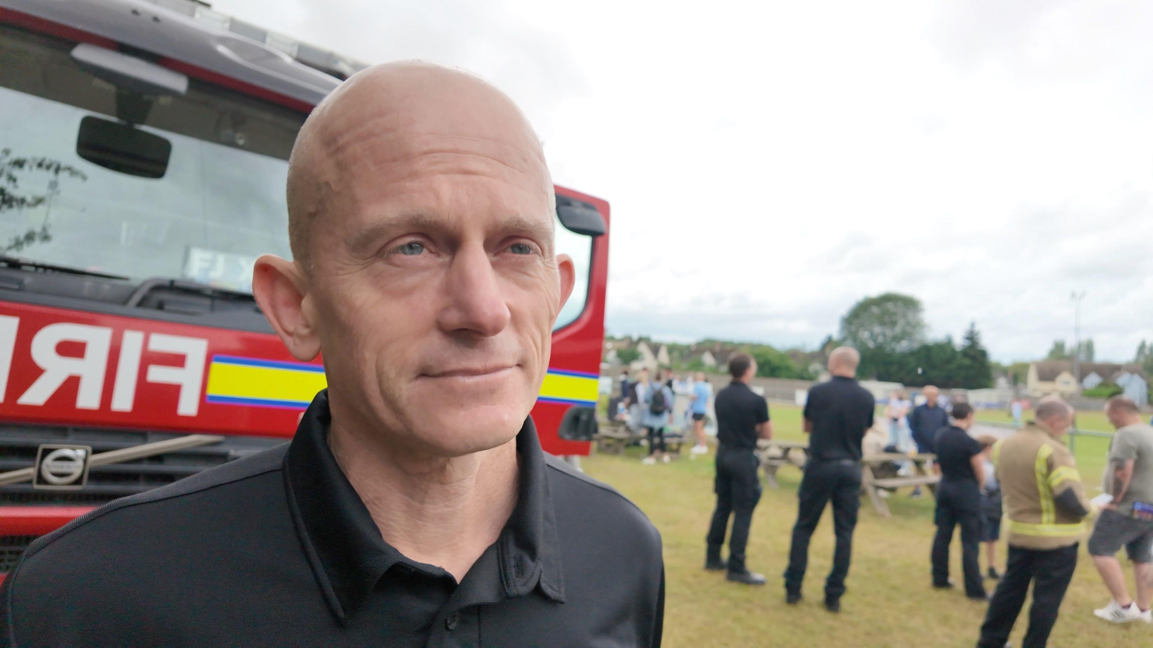 Oxfordshire's Chief Fire Officer, Rob MacDougall is wearing a black t-shirt and is standing in front of a red fire engine.