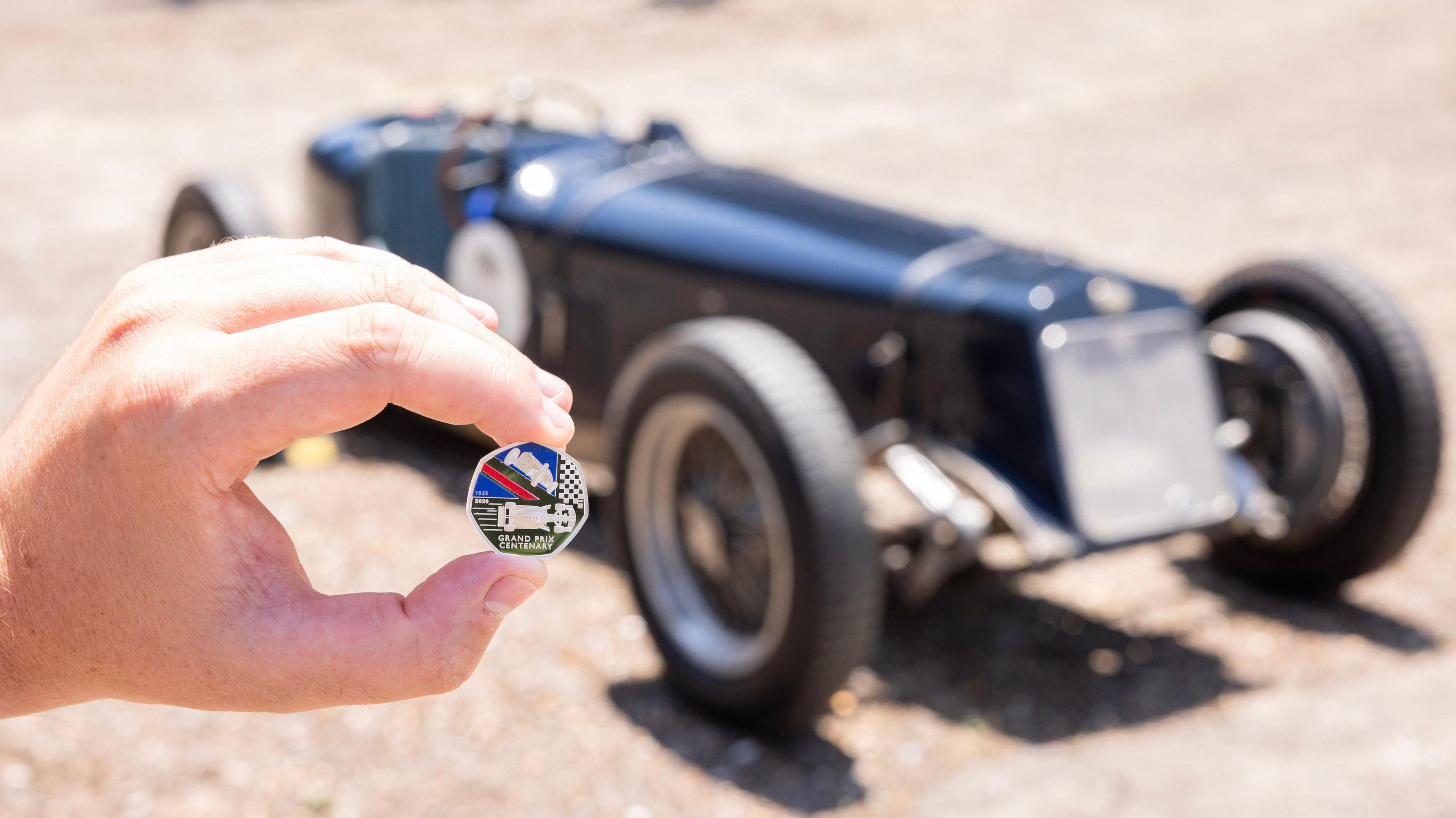 Person holding the new 50p coin in front of an historic racing car.