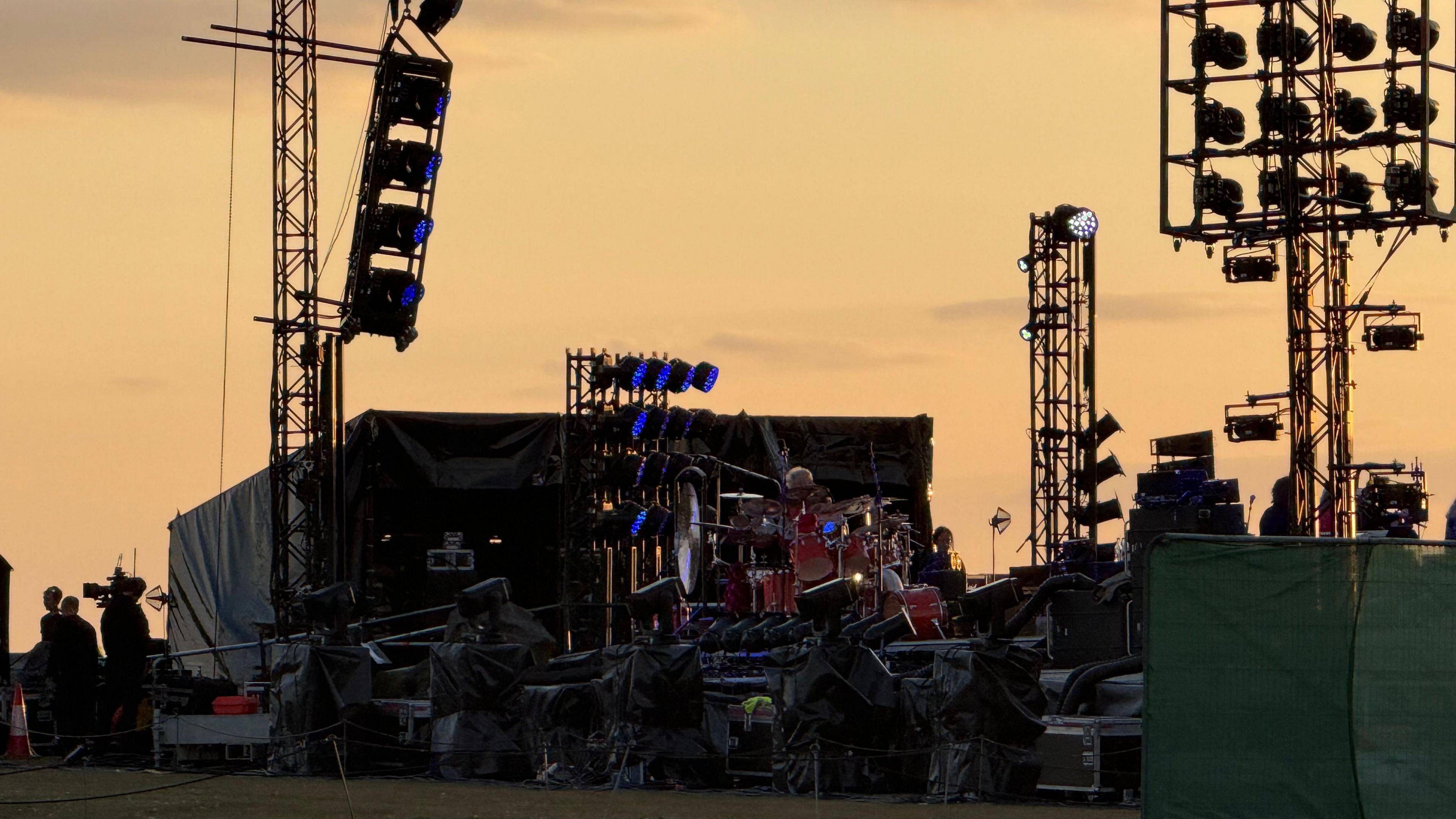 Silhouettes of a stage in the open with big lighting rigs against the sky at dusk