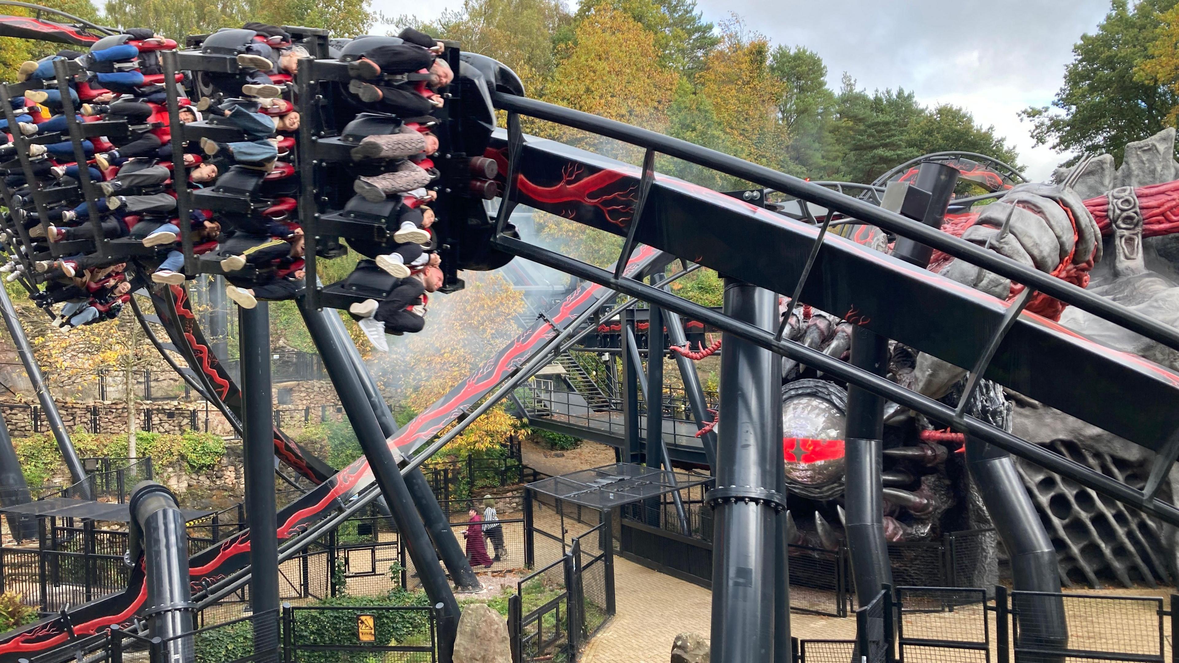 People in a carriage as it goes past on a black and red-coloured rollercoaster.