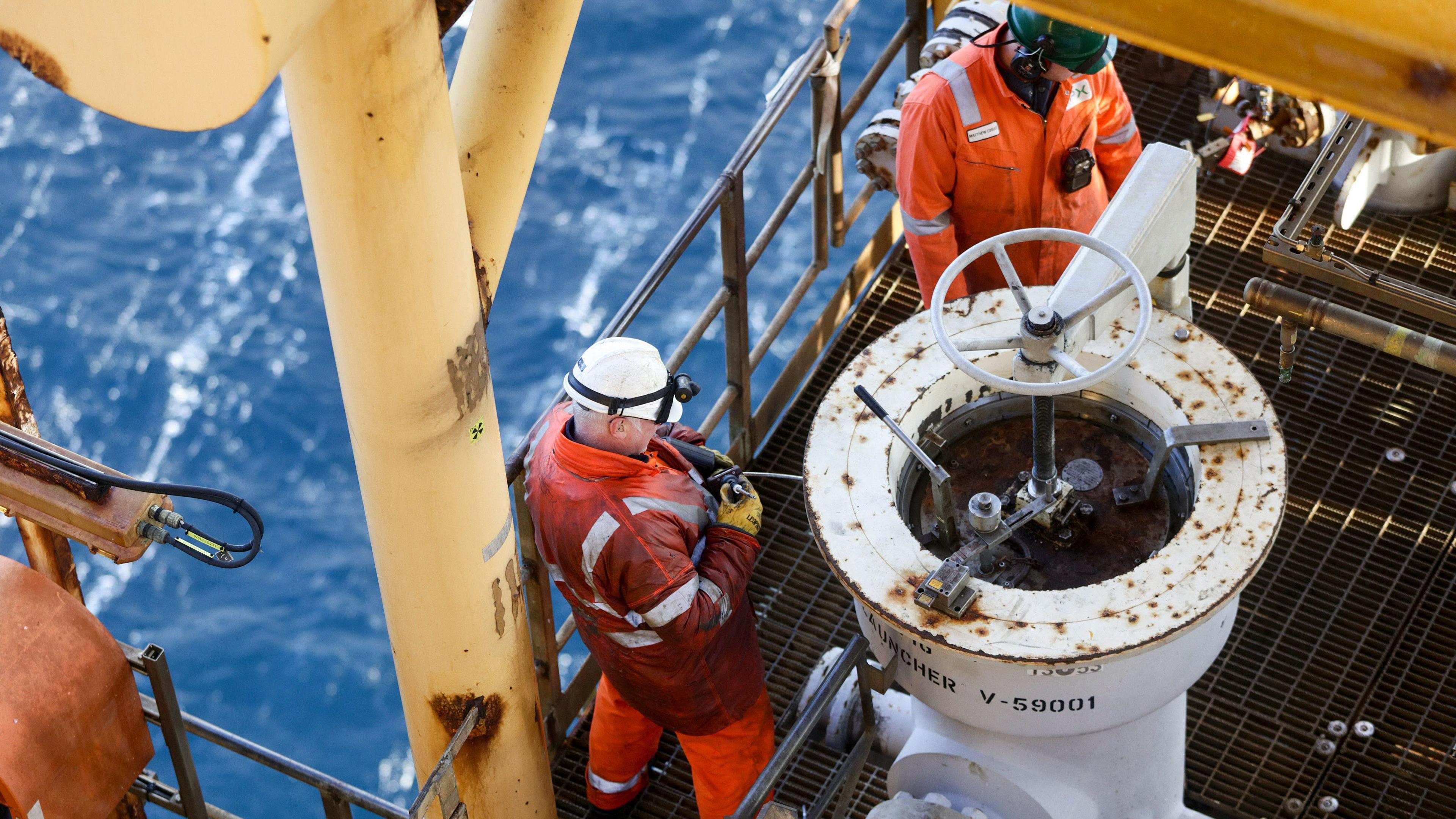 Two workers wearing orange overalls and a hard hats fix a pig launcher on the Armada gas condensate platform, operated by BG Group Plc, in the North Sea, off the coast of Aberdeen.