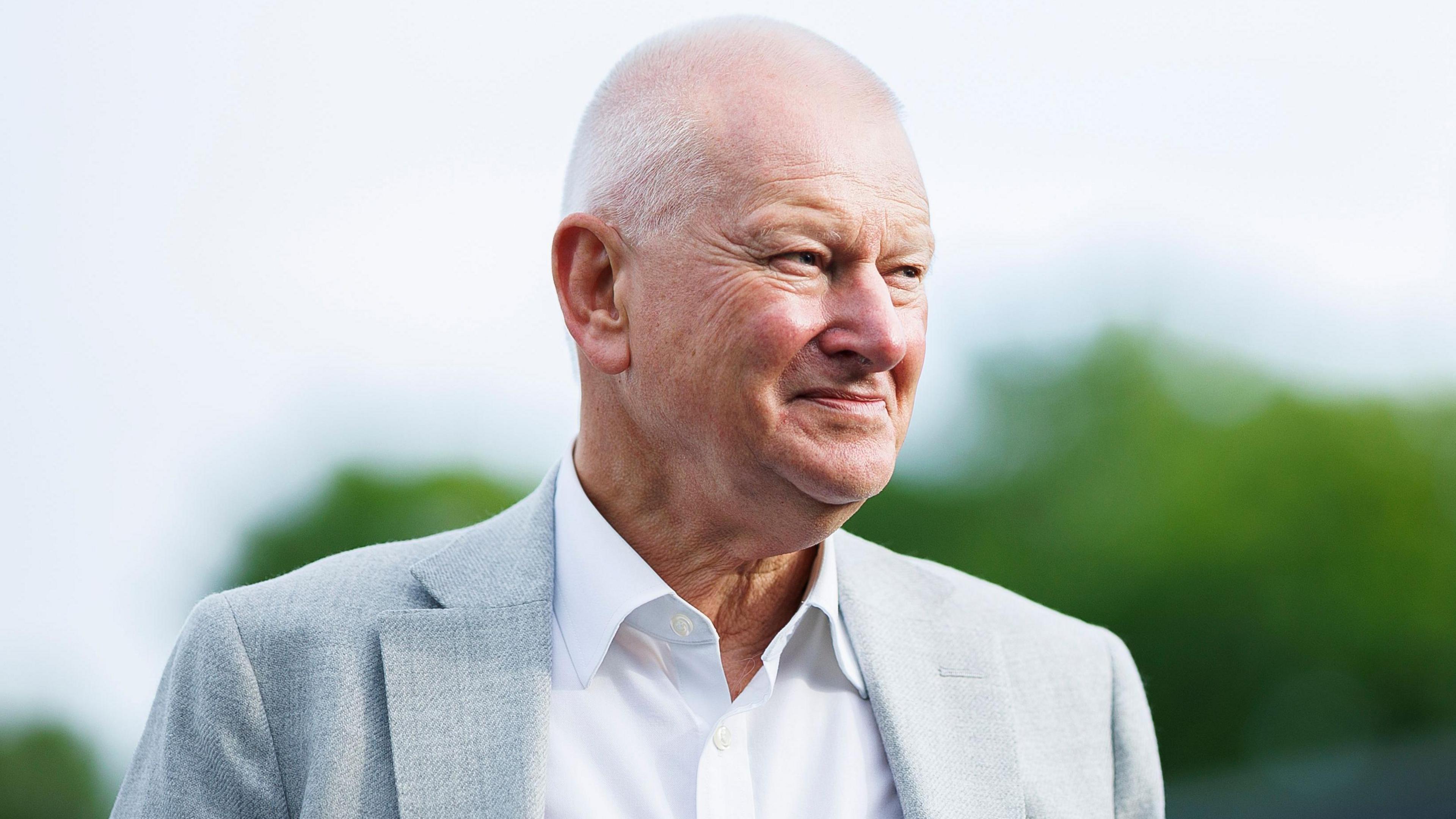 Bristol City owner Steve Lansdown with a light grey suit jacket and white shirt, with green bushes blurred in the background behind him