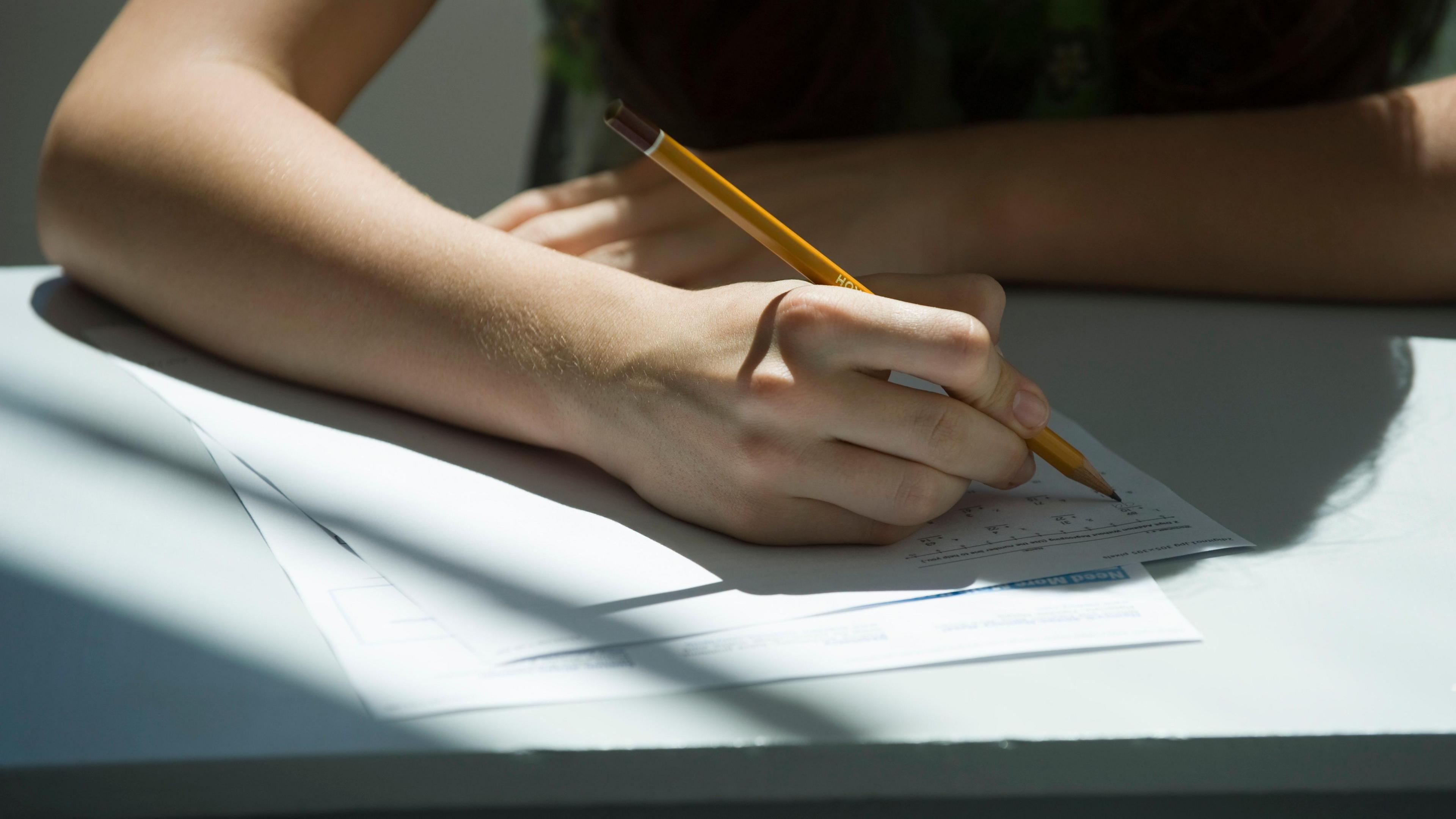 A student writes answers on a sheet with a pencil in an exam.