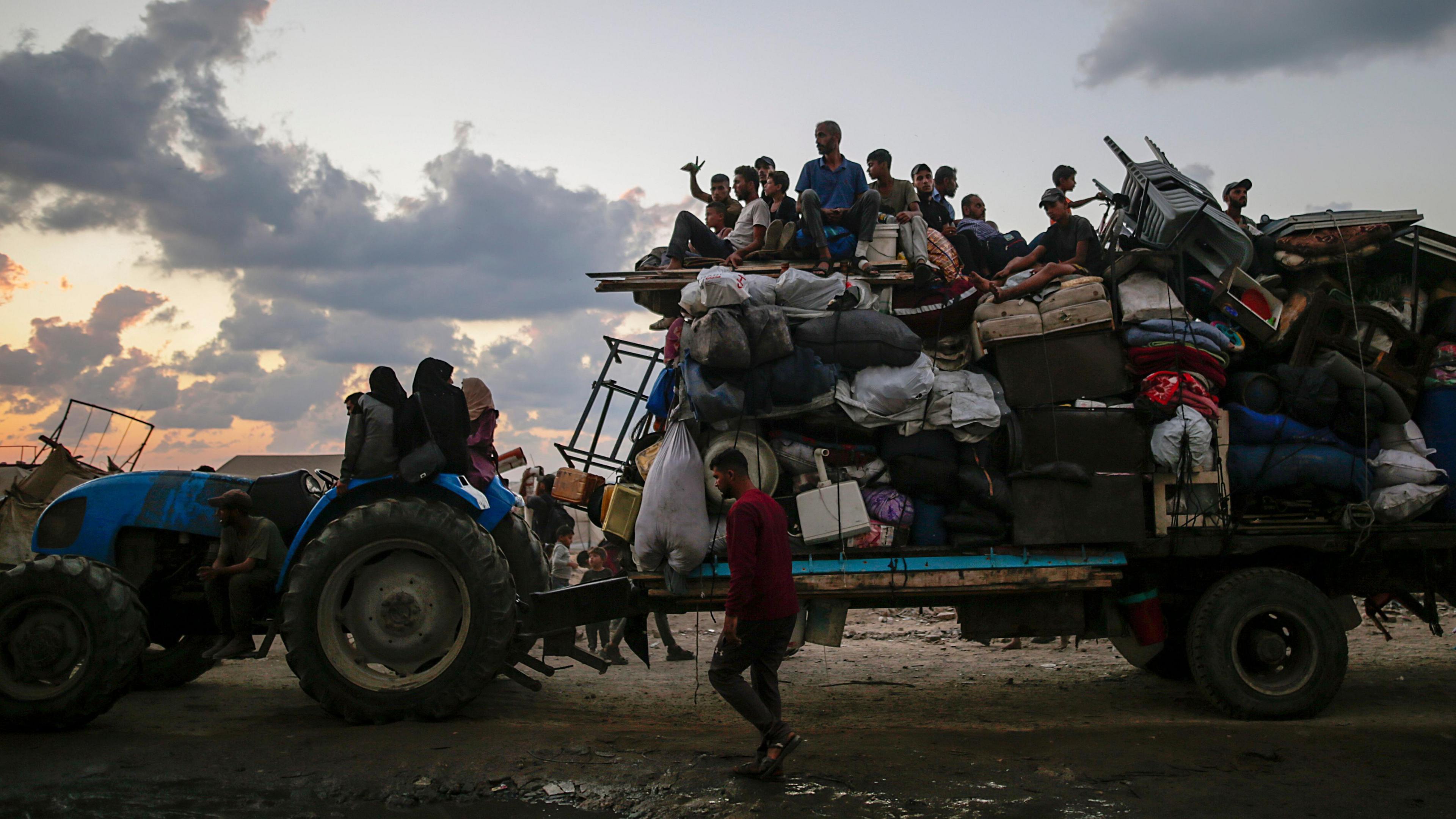 A tractor tows a large truck filled with belongings and people. 